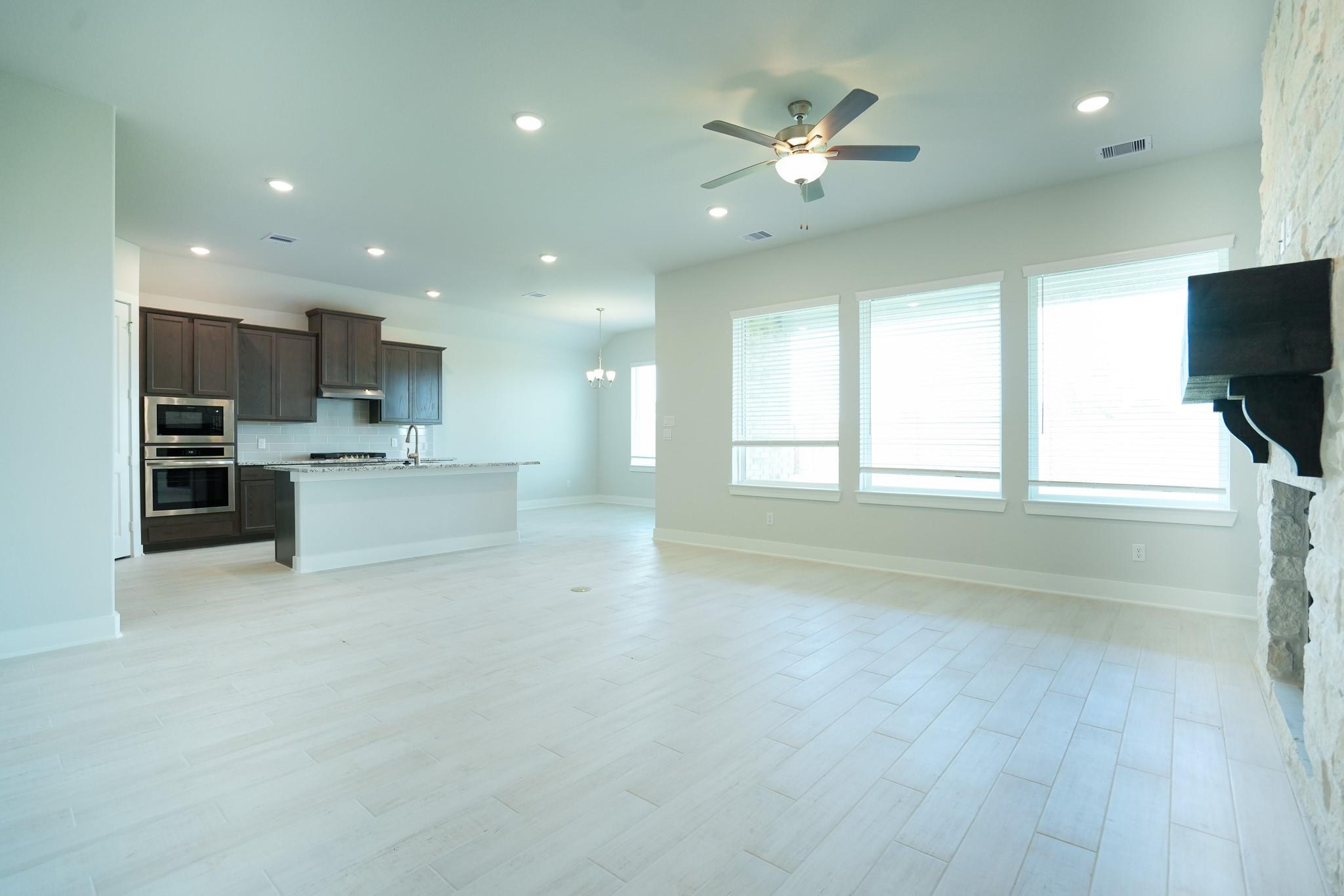 Open-concept kitchen-living area with dark cabinets, double ovens, island, large windows, and stone wall in Davidson Homes The Edward C, Lago Mar