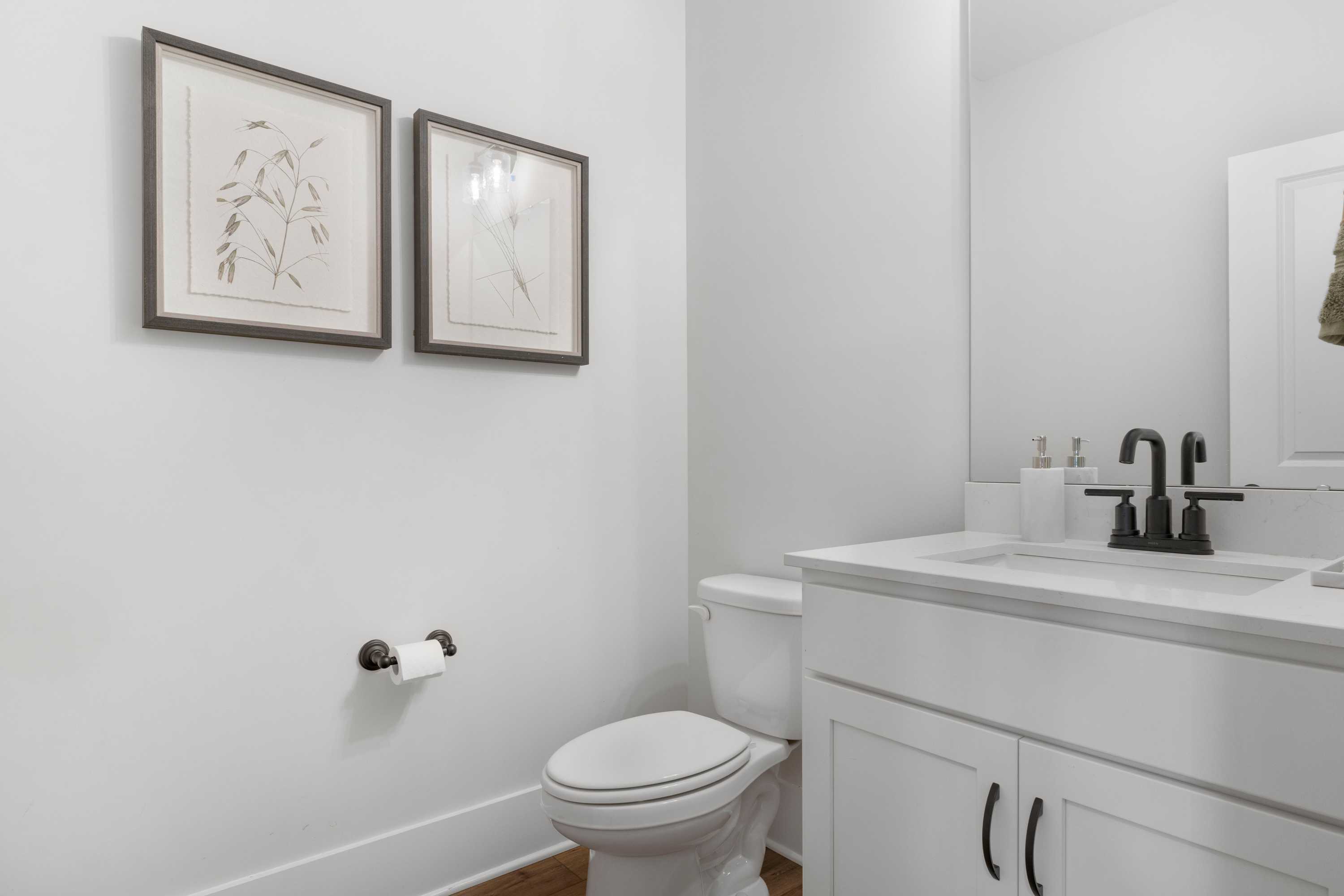 Modern powder room in Briercreek, Meridianville AL with white shaker vanity, matte black faucet, framed botanical art, and toilet