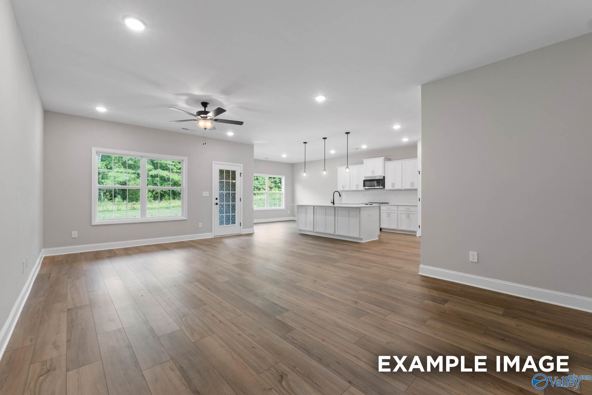 Open-concept living-kitchen with hardwood floors, large windows, white island cabinets, and ceiling fan in Davidson Homes The Montgomery B, Toney, Alabama