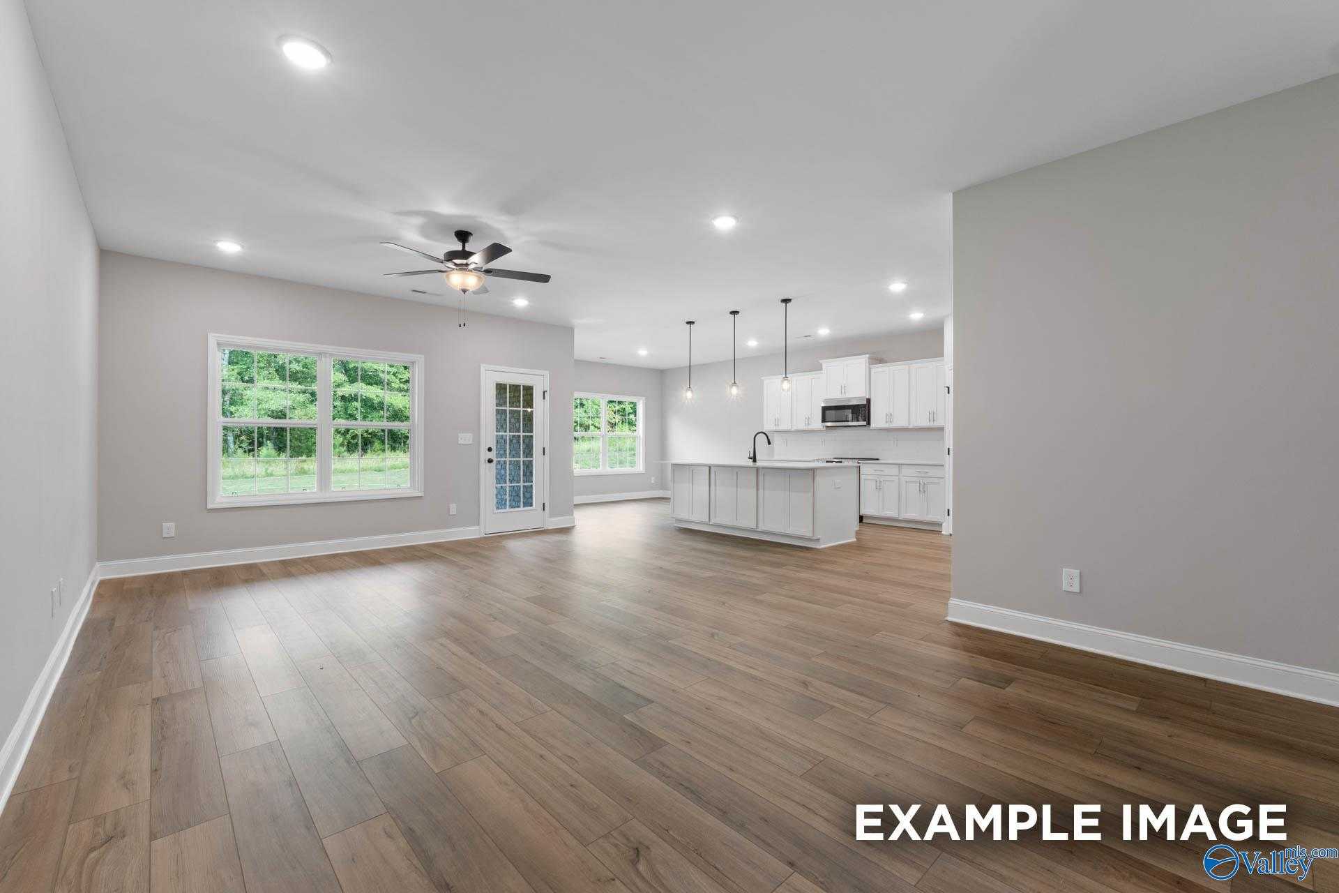 Open-concept living-kitchen with hardwood floors, large windows, white island cabinets, and ceiling fan in Davidson Homes The Montgomery B, Toney, Alabama