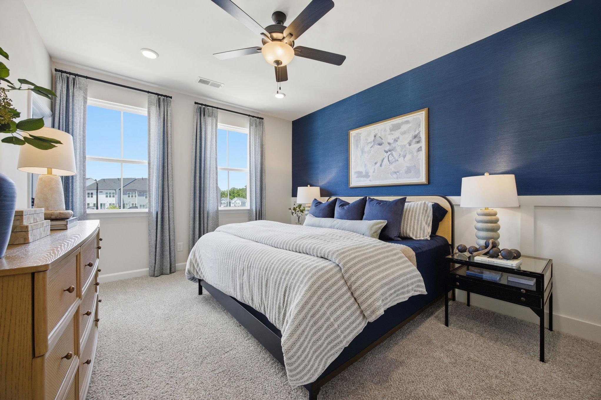 Spacious bedroom interior at Forestville Yard in Knightdale NC with navy accent wall, striped bedding, ceiling fan, and large windows