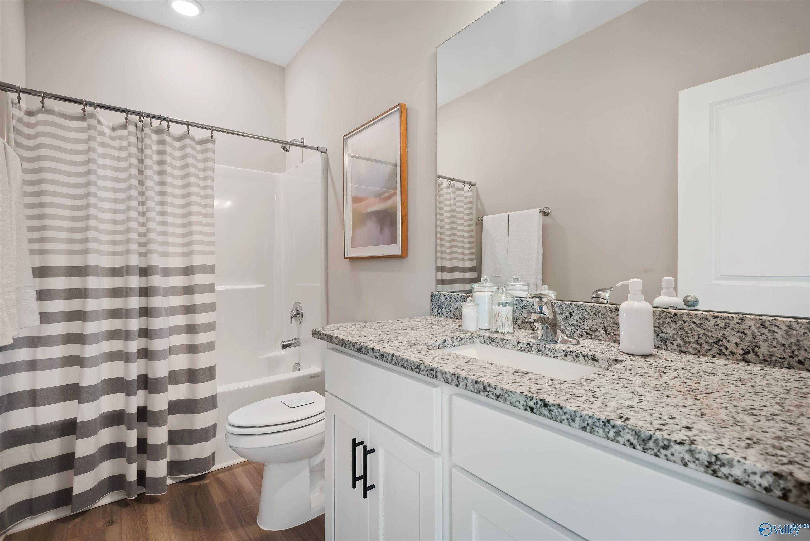 Modern bathroom with granite vanity, striped curtain shower, white toilet, and neutral tones in Davidson Homes The Daphne, Harvest, Alabama