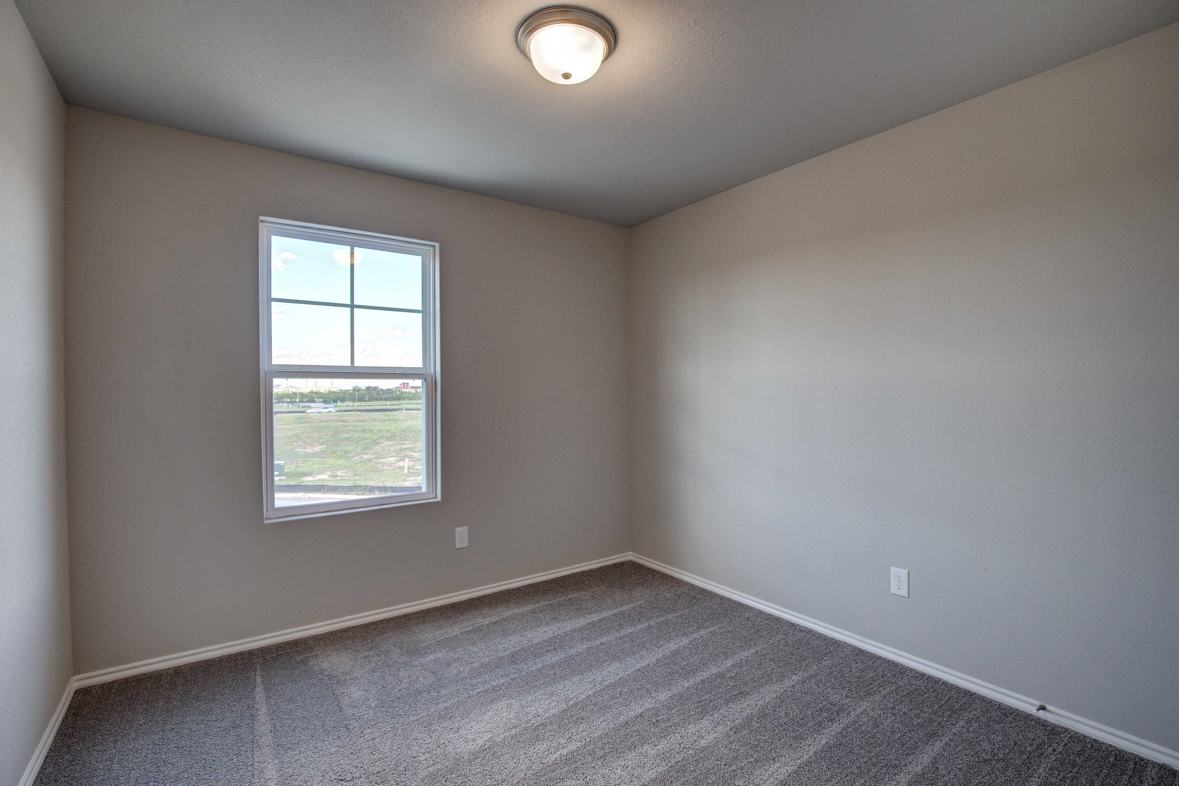 Spacious secondary bedroom in The Blanco B with beige walls, gray carpet, large window overlooking fields, and ceiling light