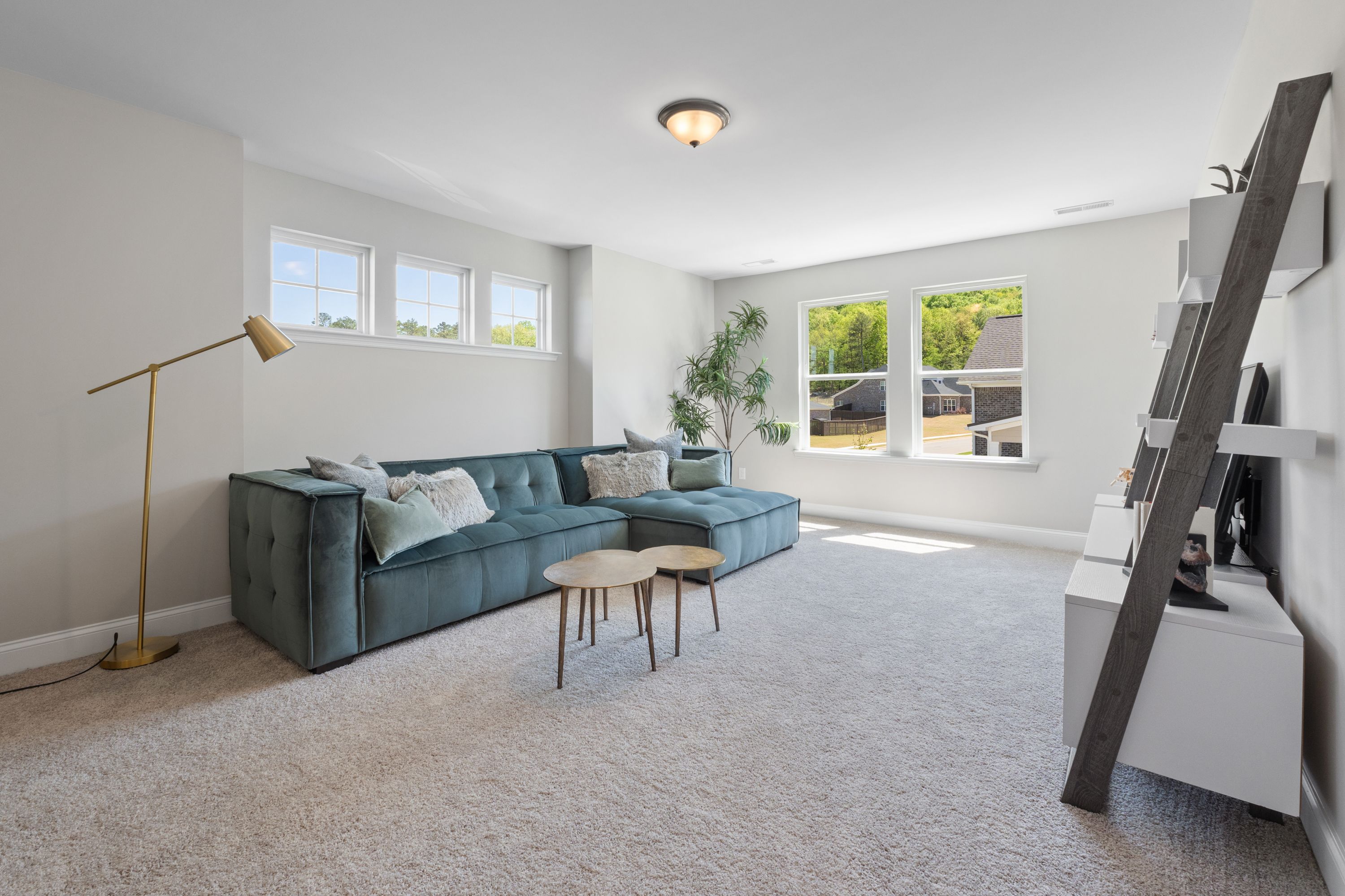 Cozy living room in The Haven D home design with teal velvet L-shaped sofa, ladder shelf, and large windows
