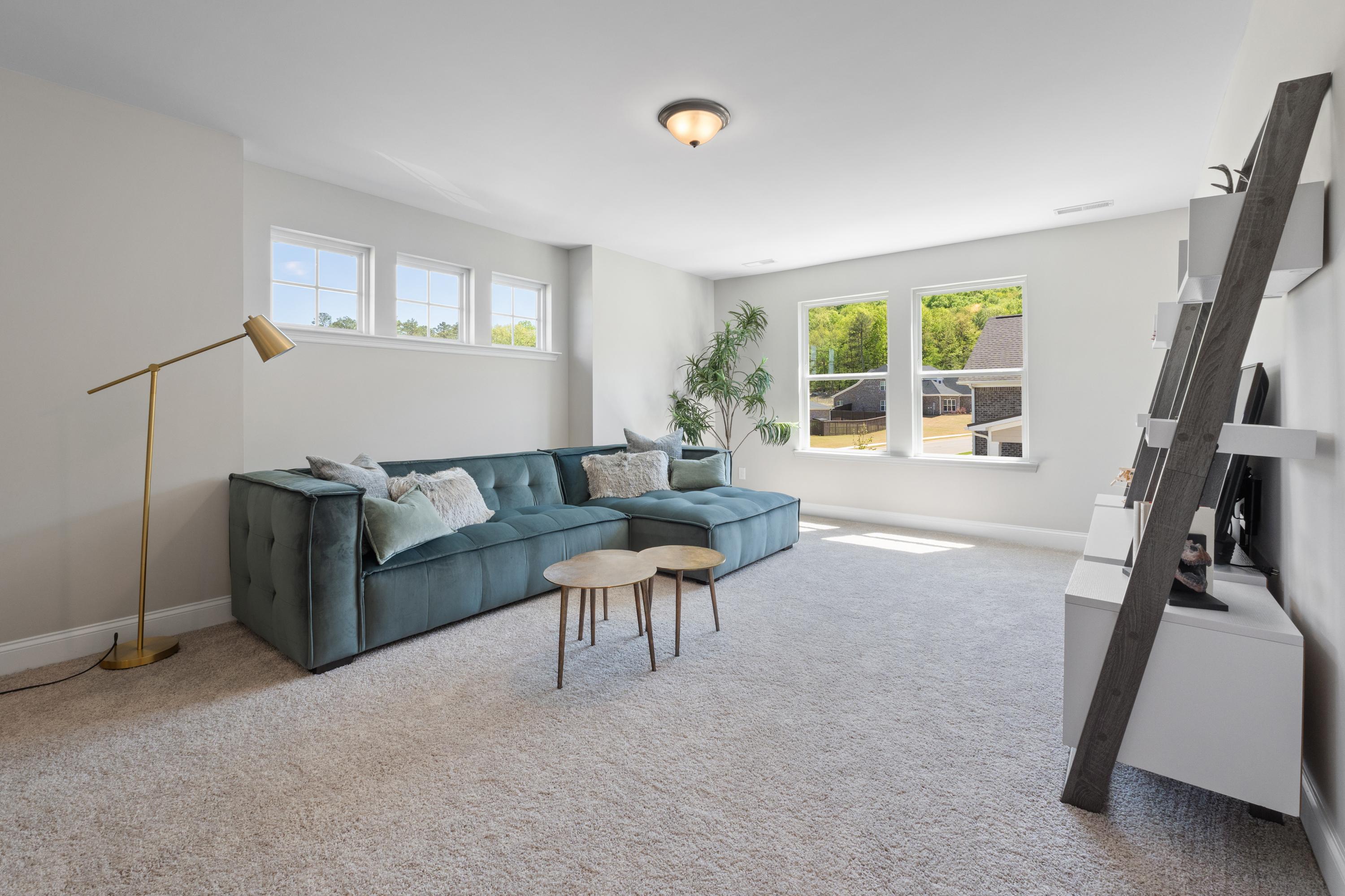 Cozy living room in The Haven D home design with teal velvet L-shaped sofa, ladder shelf, and large windows