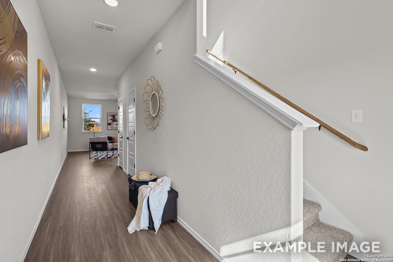 Bright hallway with light wood floors, white staircase railing, abstract wall art, and coastal accents in Davidson Homes The Trinity B, San Antonio