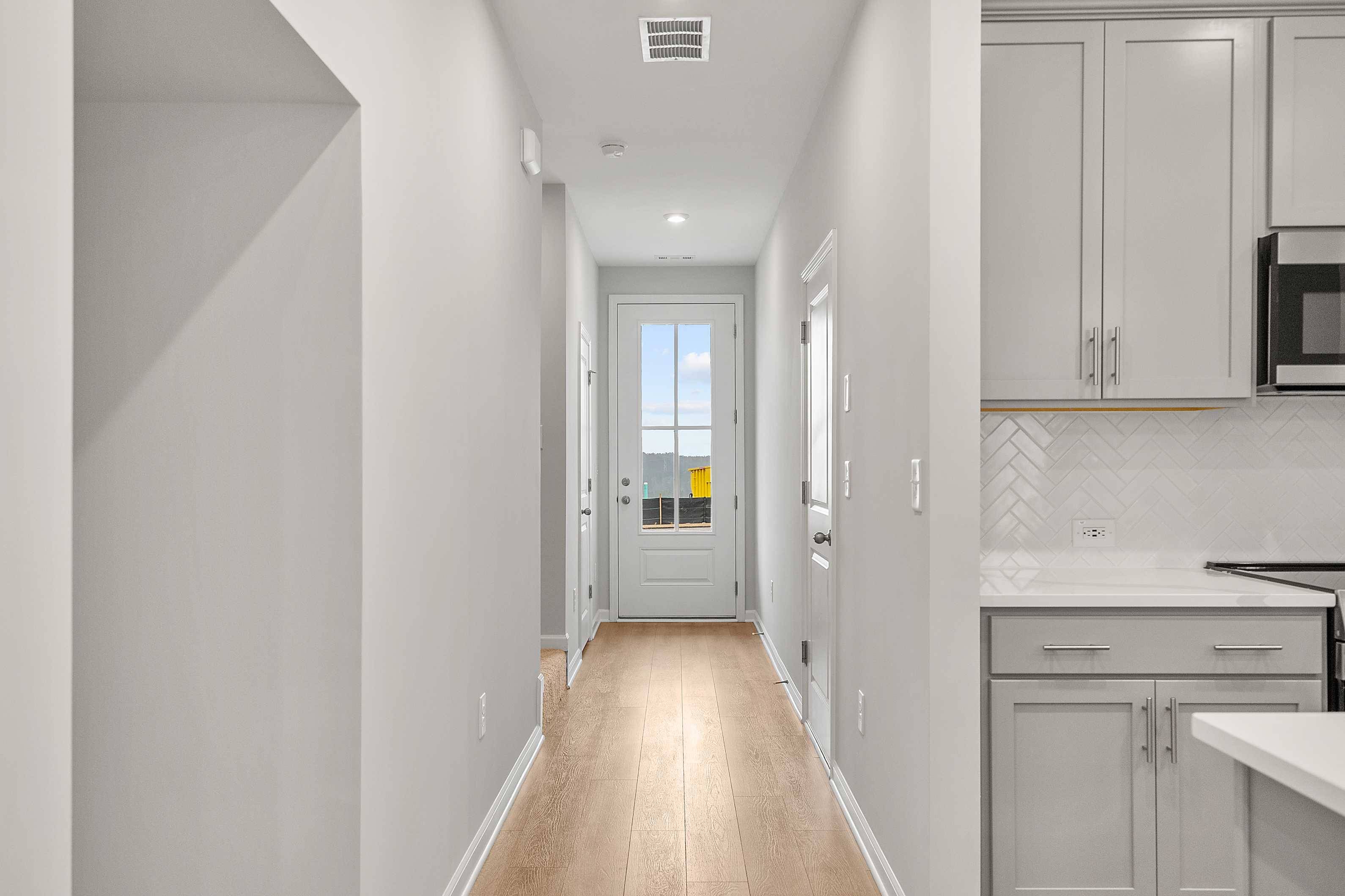 Spacious hallway with hardwood floors leading to glass door in The Durant A home, adjacent gray kitchen cabinets and subway tile backsplash