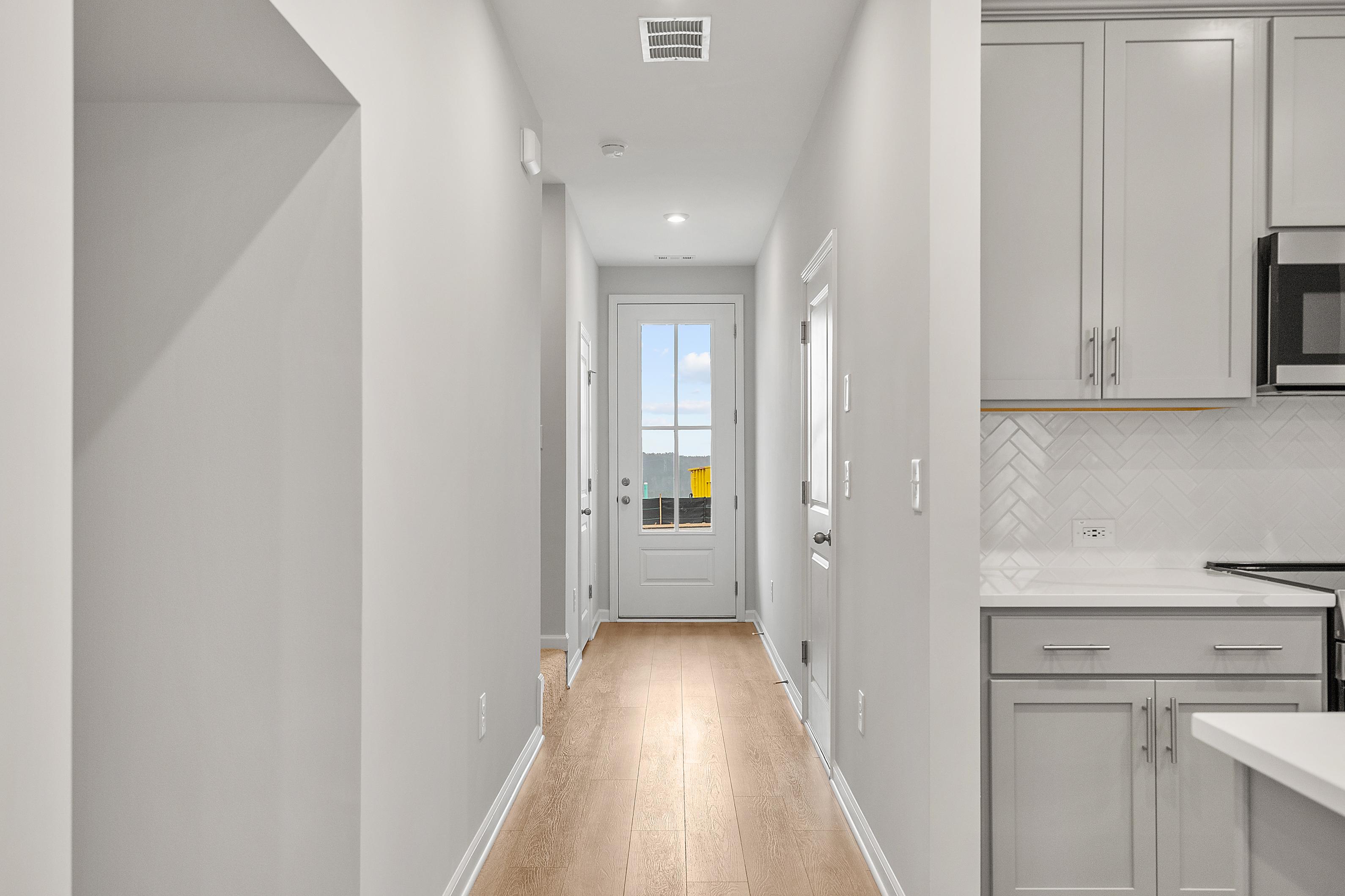 Spacious hallway with hardwood floors leading to glass door in The Durant A home, adjacent gray kitchen cabinets and subway tile backsplash
