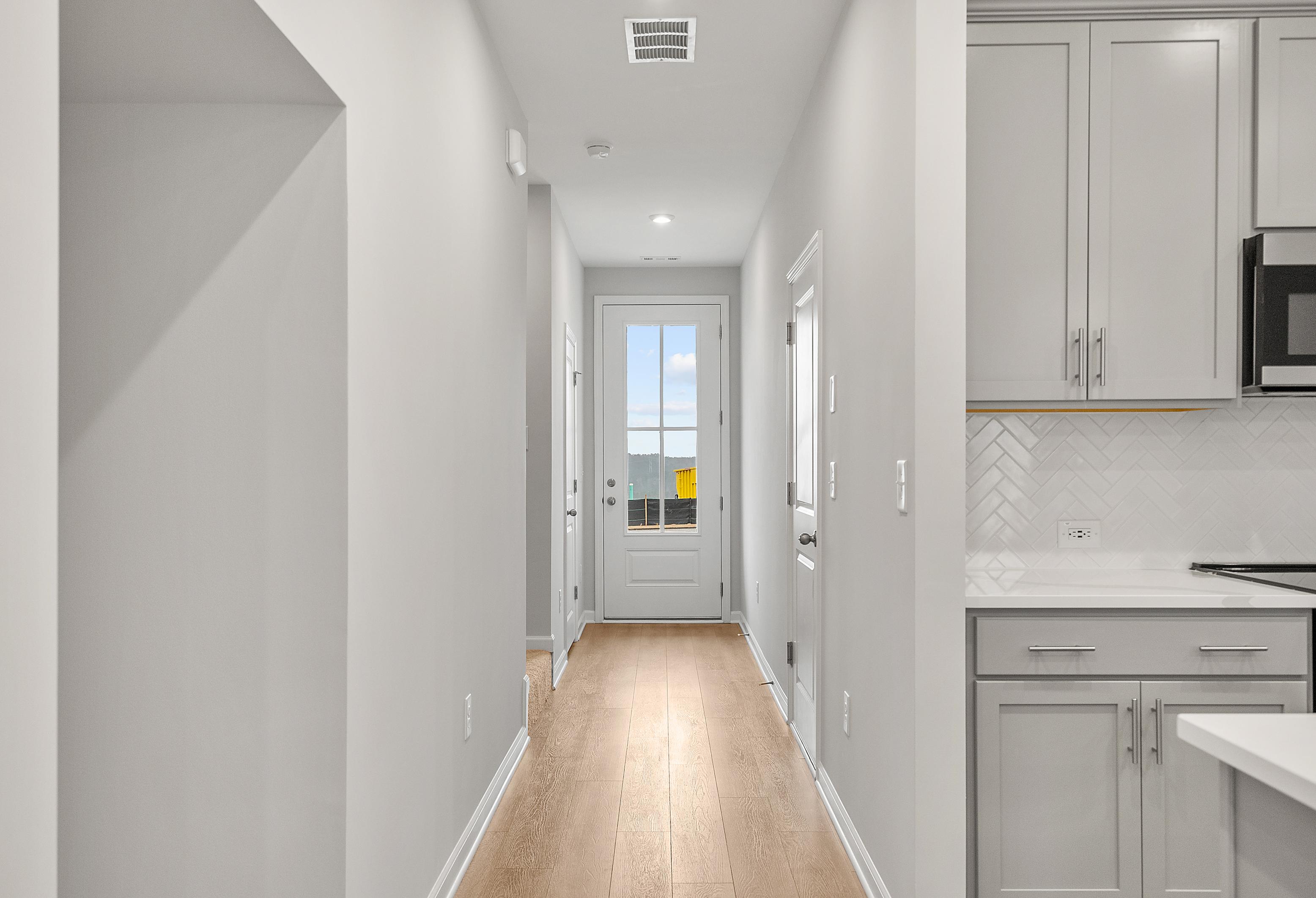 Spacious hallway with hardwood floors leading to glass door in The Durant A home, adjacent gray kitchen cabinets and subway tile backsplash