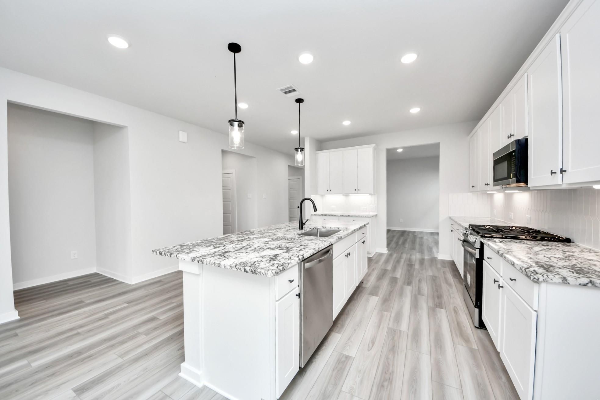 Modern white kitchen with granite island and stainless appliances in The Sorrento E floor plan at Sundance Cove, Crosby.