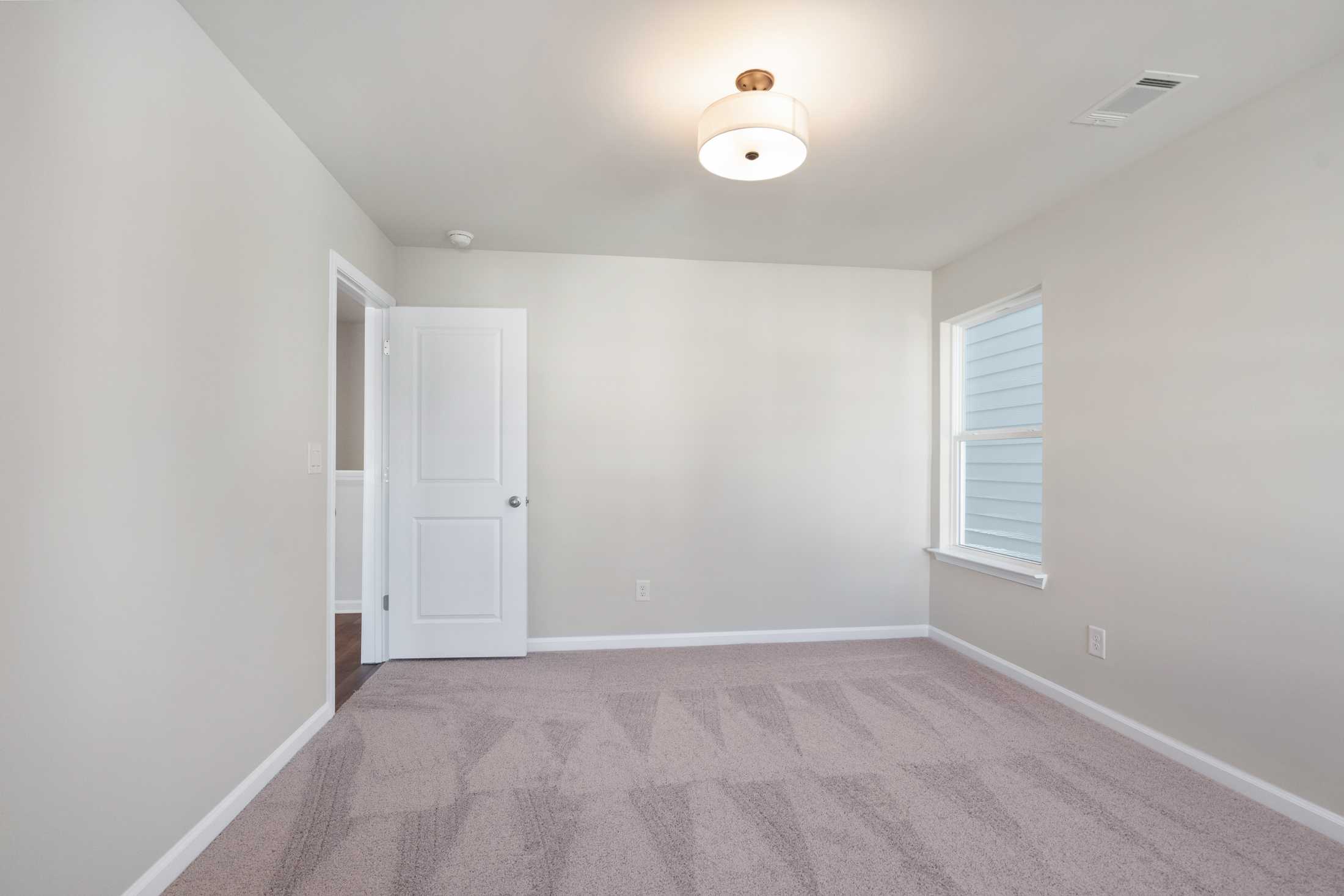 Spacious upper-floor bedroom in The Cary B with beige walls, tan carpet, white door, window blinds, and ceiling light