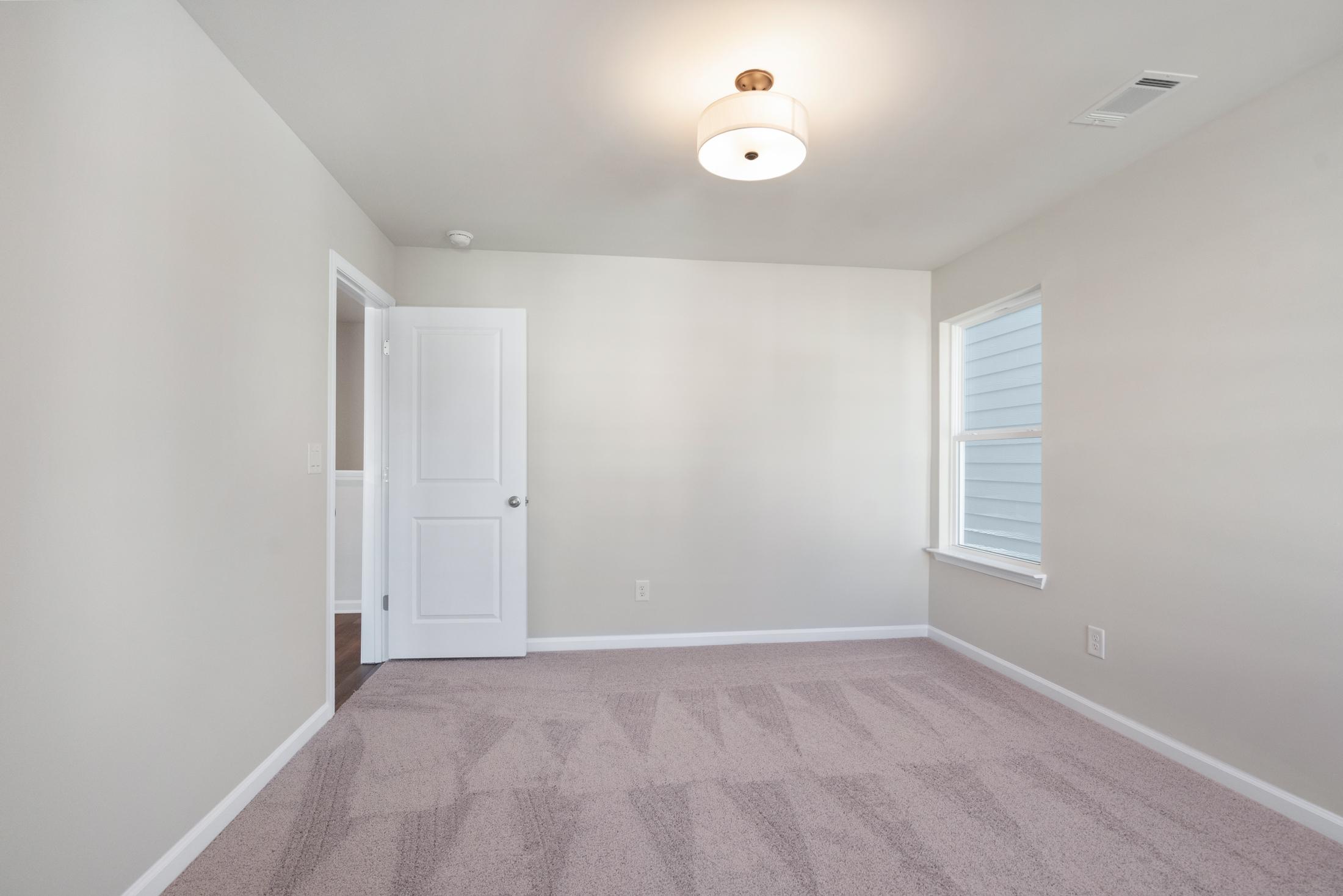 Spacious upper-floor bedroom in The Cary B with beige walls, tan carpet, white door, window blinds, and ceiling light