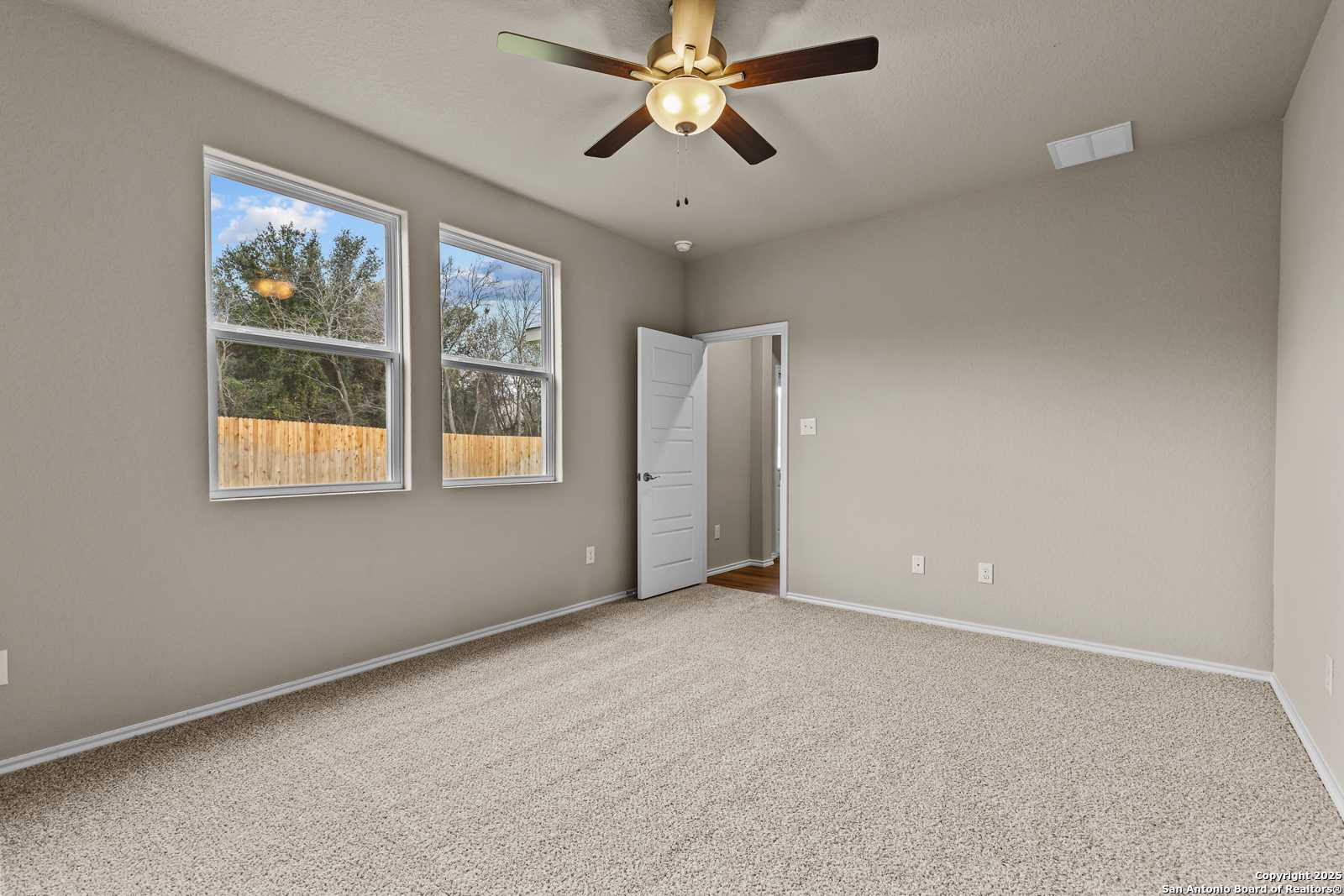 Bright secondary bedroom with neutral walls, carpet flooring, large windows, and ceiling fan in Davidson Homes The Douglas F, San Antonio