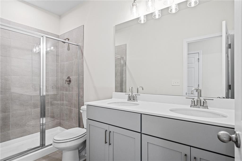 Modern bathroom with dual vanity, gray cabinets, and tiled glass shower in The Glenwood A at Wehunt Meadows, Hoschton.
