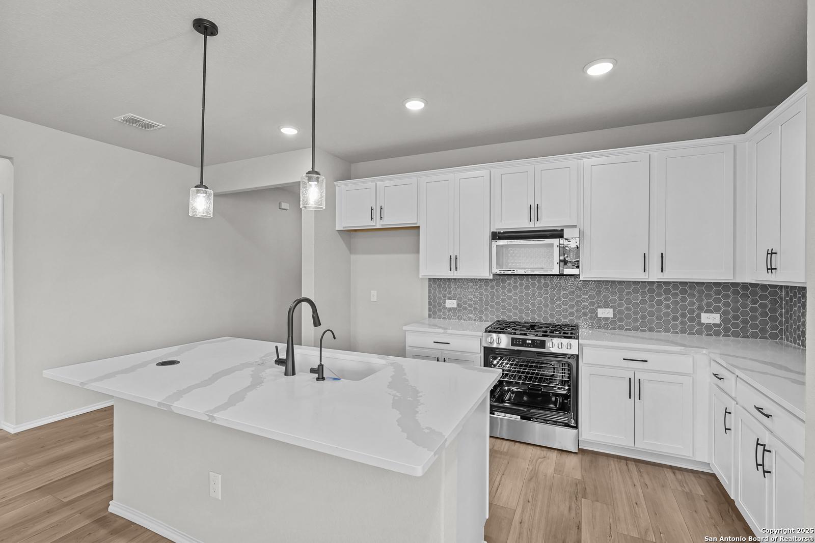 Modern white kitchen with quartz island sink, stainless gas range, and cabinets in The Daphne K 4-bedroom home, San Antonio