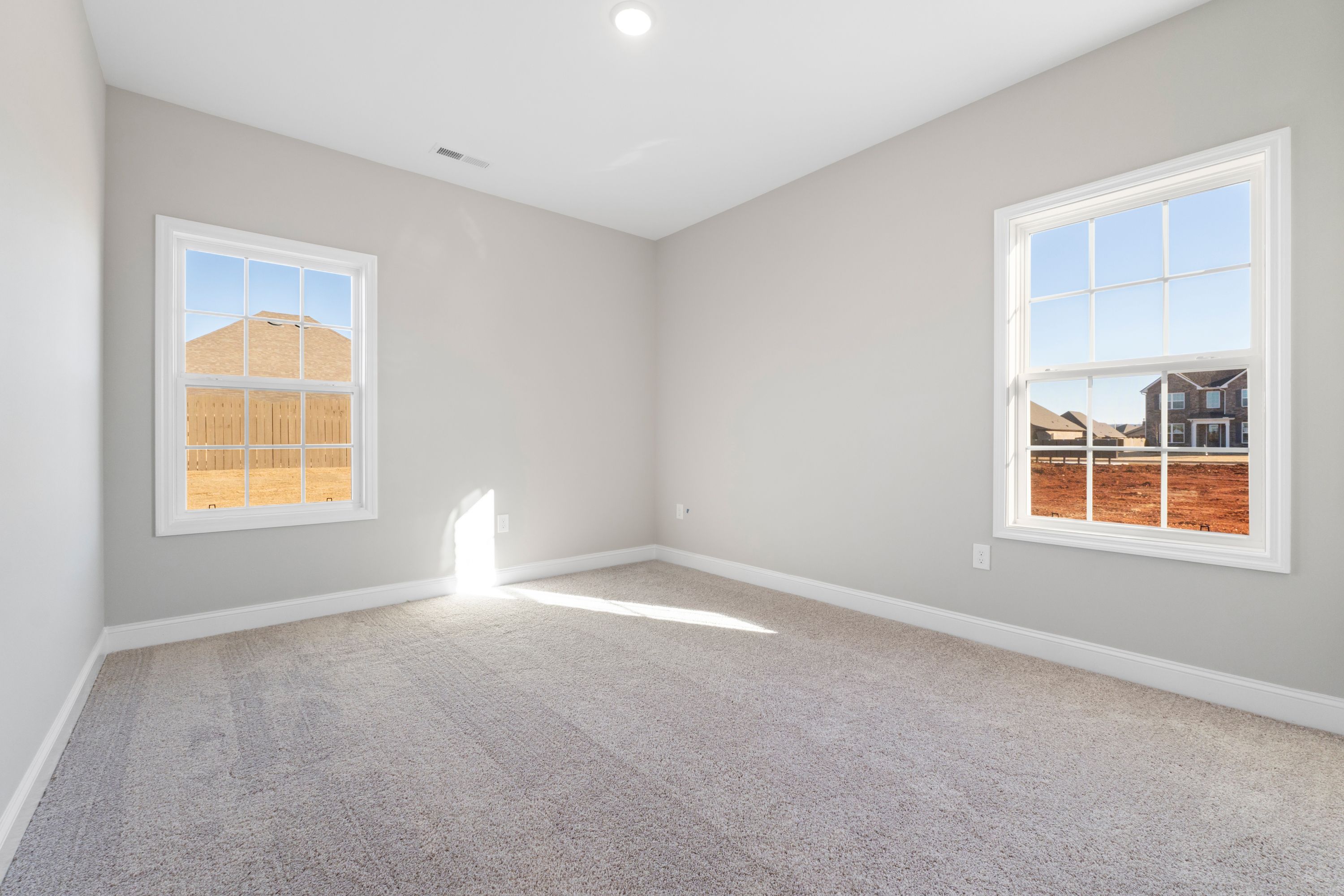 Spacious bedroom in The Valencia home design with light gray walls, beige carpet, large windows overlooking new construction site
