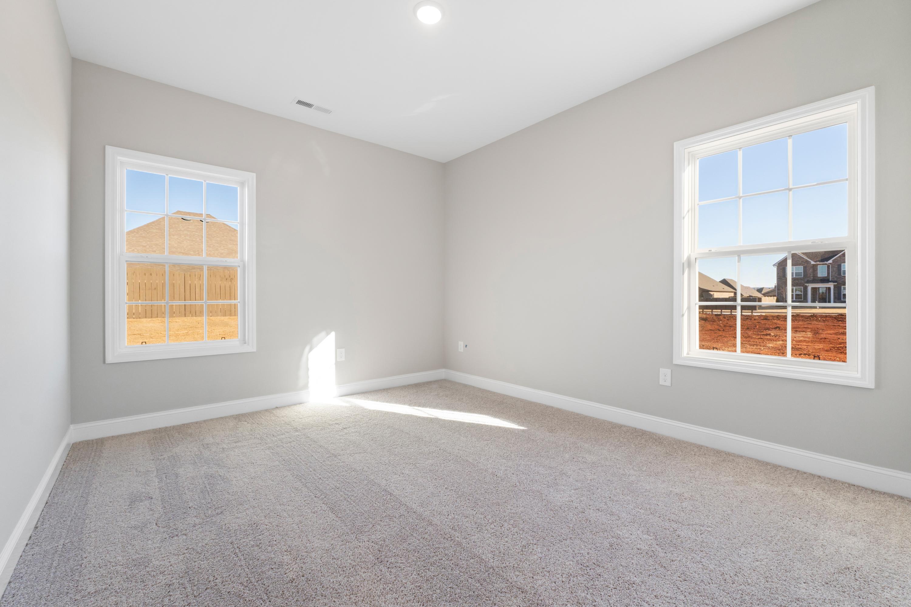 Spacious bedroom in The Valencia home design with light gray walls, beige carpet, large windows overlooking new construction site