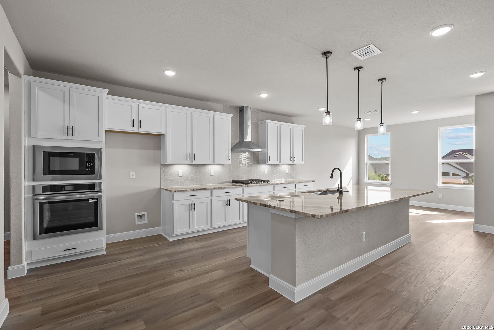 White shaker kitchen with granite island, stainless appliances, and pendant lights in Davidson Homes The Foster E, Castroville, Texas