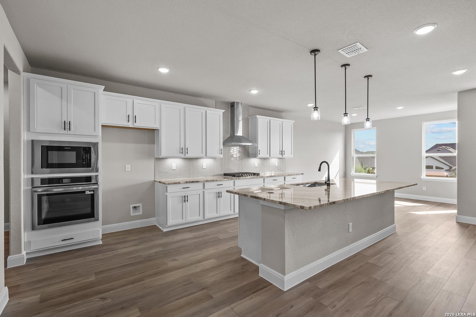 White shaker kitchen with granite island, stainless appliances, and pendant lights in Davidson Homes The Foster E, Castroville, Texas