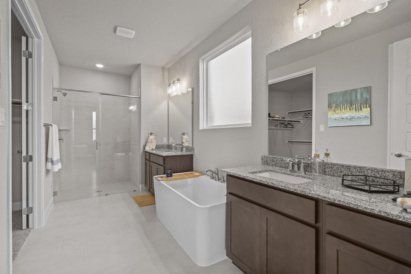 Master bath in The Jennings G featuring a soaking tub, glass-enclosed shower, dual vanities, and granite countertops.