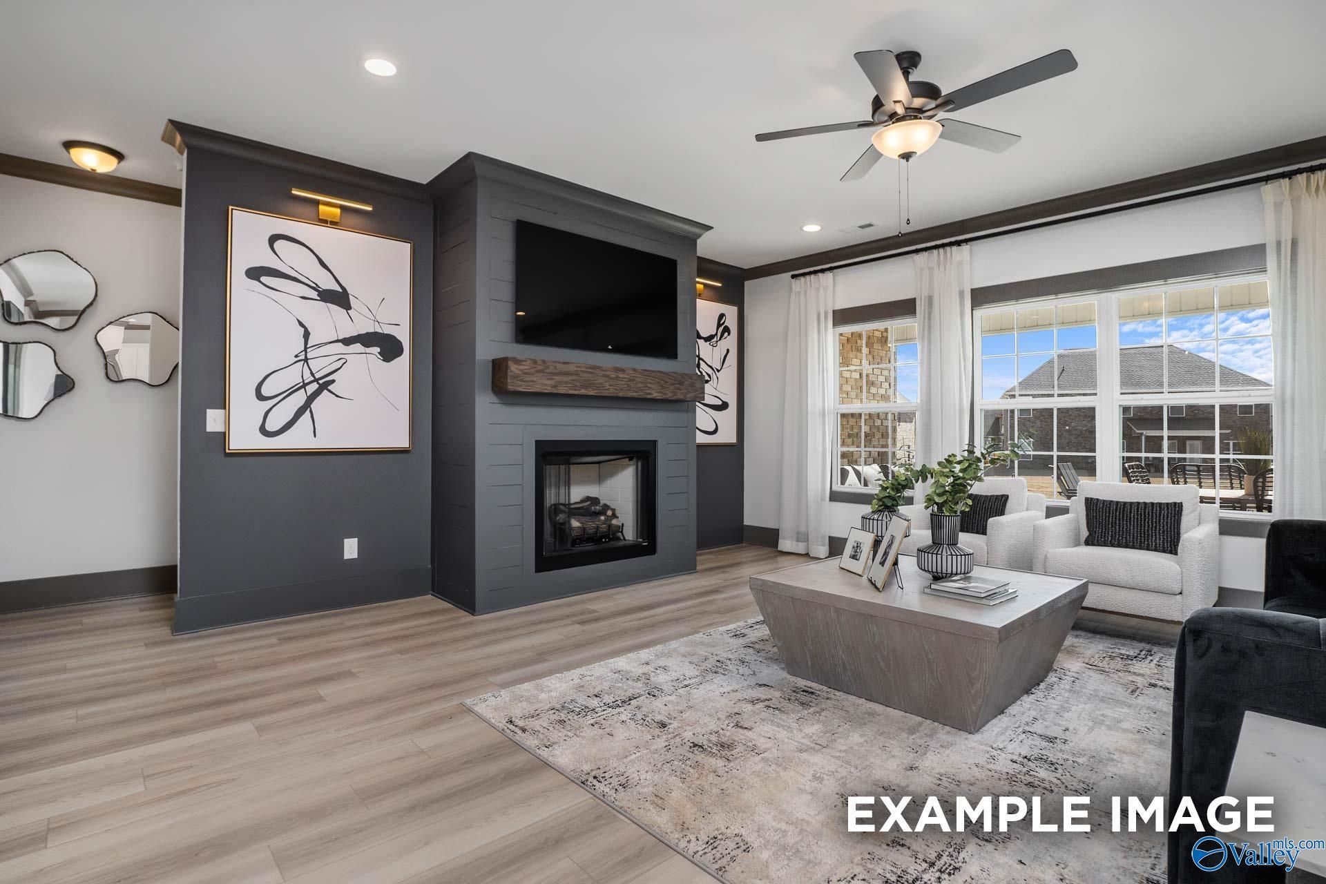 Cozy living room with brick fireplace, mounted TV, abstract wall art, white sofa, and large windows in Davidson Homes The Rockford B, Madison, Alabama