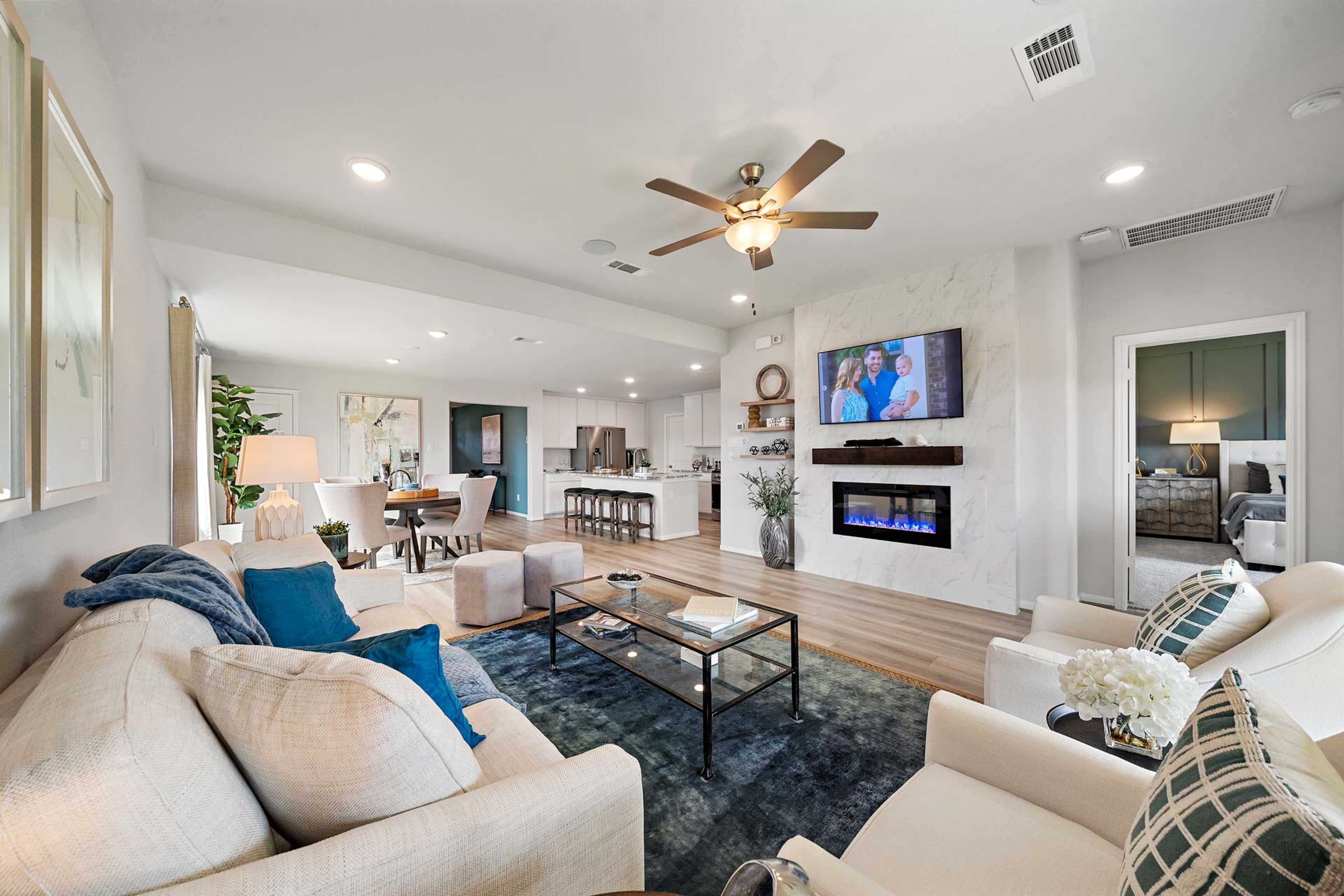 Open-concept living room in Sunterra Katy Texas by Davidson Homes with gas fireplace TV dining area and modern seating