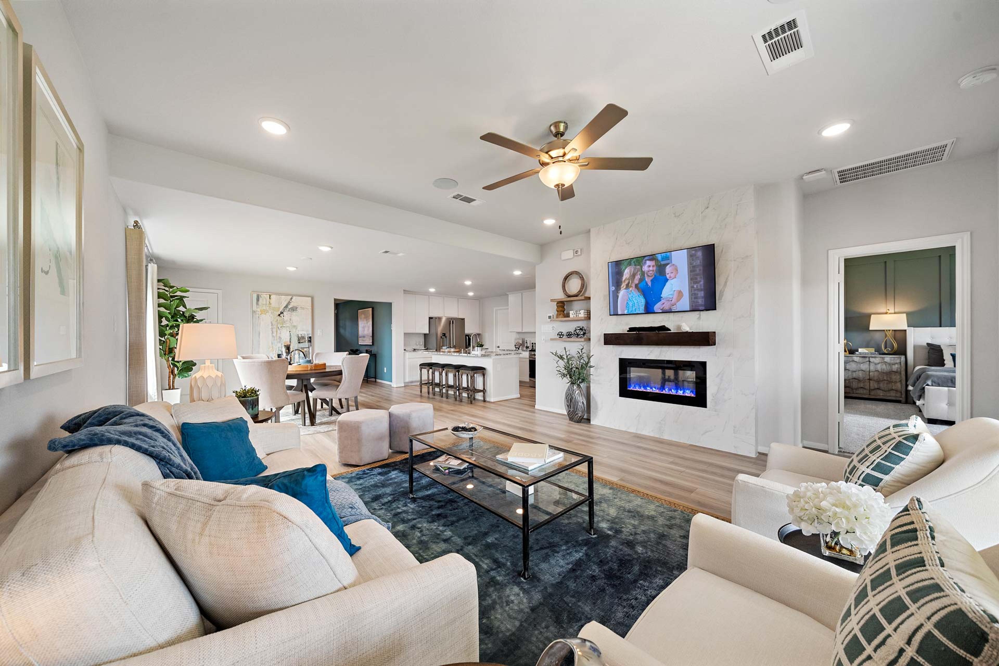 Open-concept living room in Sunterra Katy Texas by Davidson Homes with gas fireplace TV dining area and modern seating