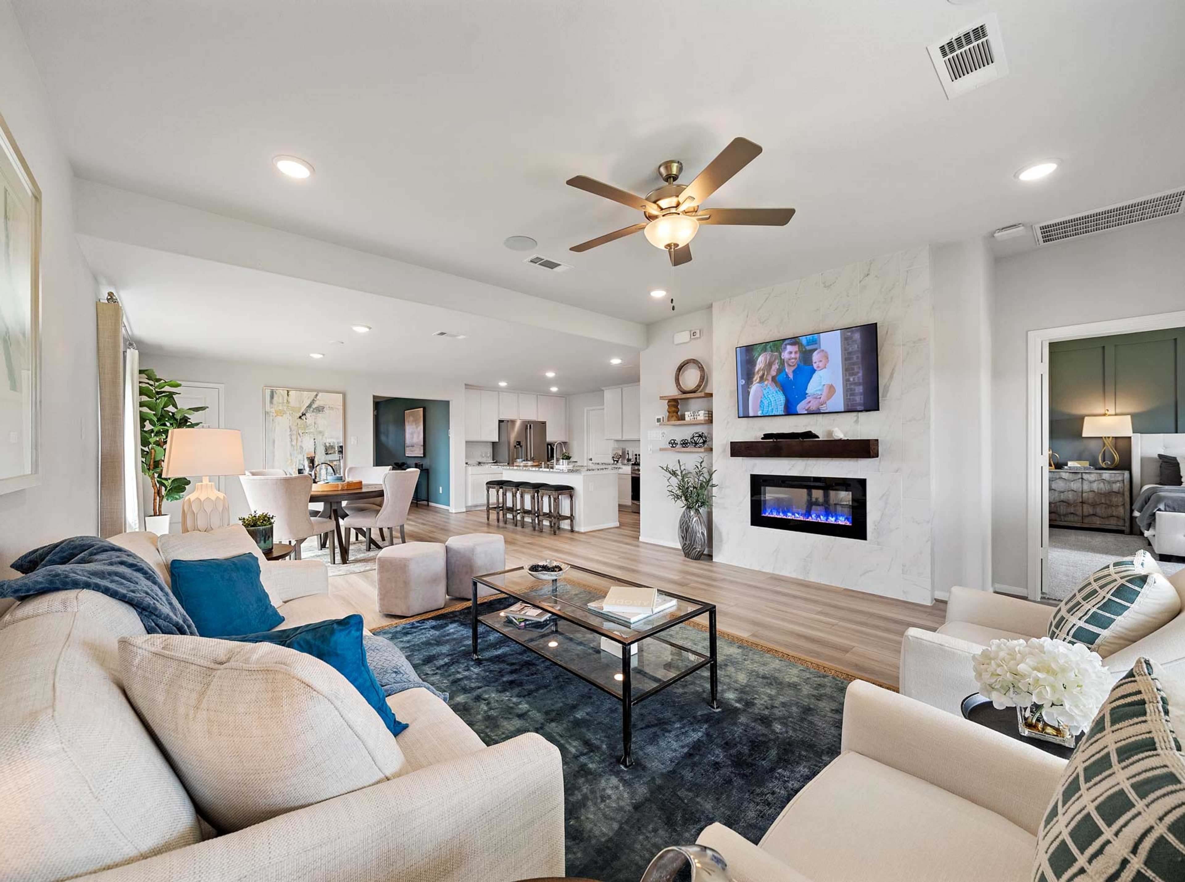 Open-concept living room in Sunterra Katy Texas by Davidson Homes with gas fireplace TV dining area and modern seating