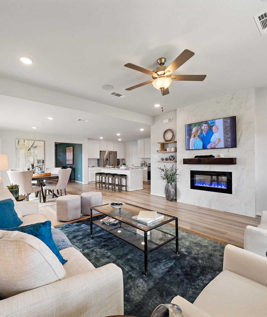 Open-concept living room in Sunterra Katy Texas by Davidson Homes with gas fireplace TV dining area and modern seating
