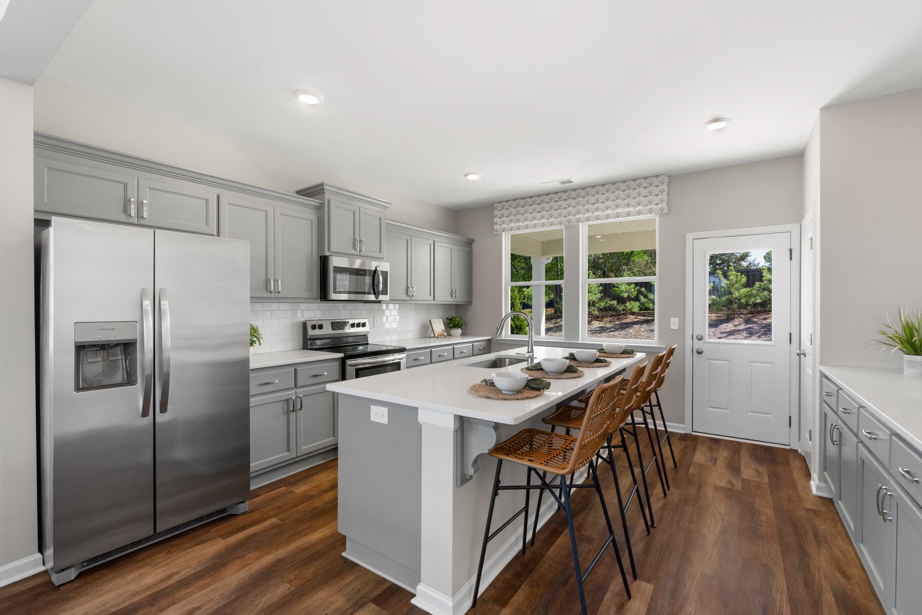Spacious modern kitchen in Evergreen Mill Madison AL with gray cabinets, quartz island bar seating, stainless appliances, hardwood floors