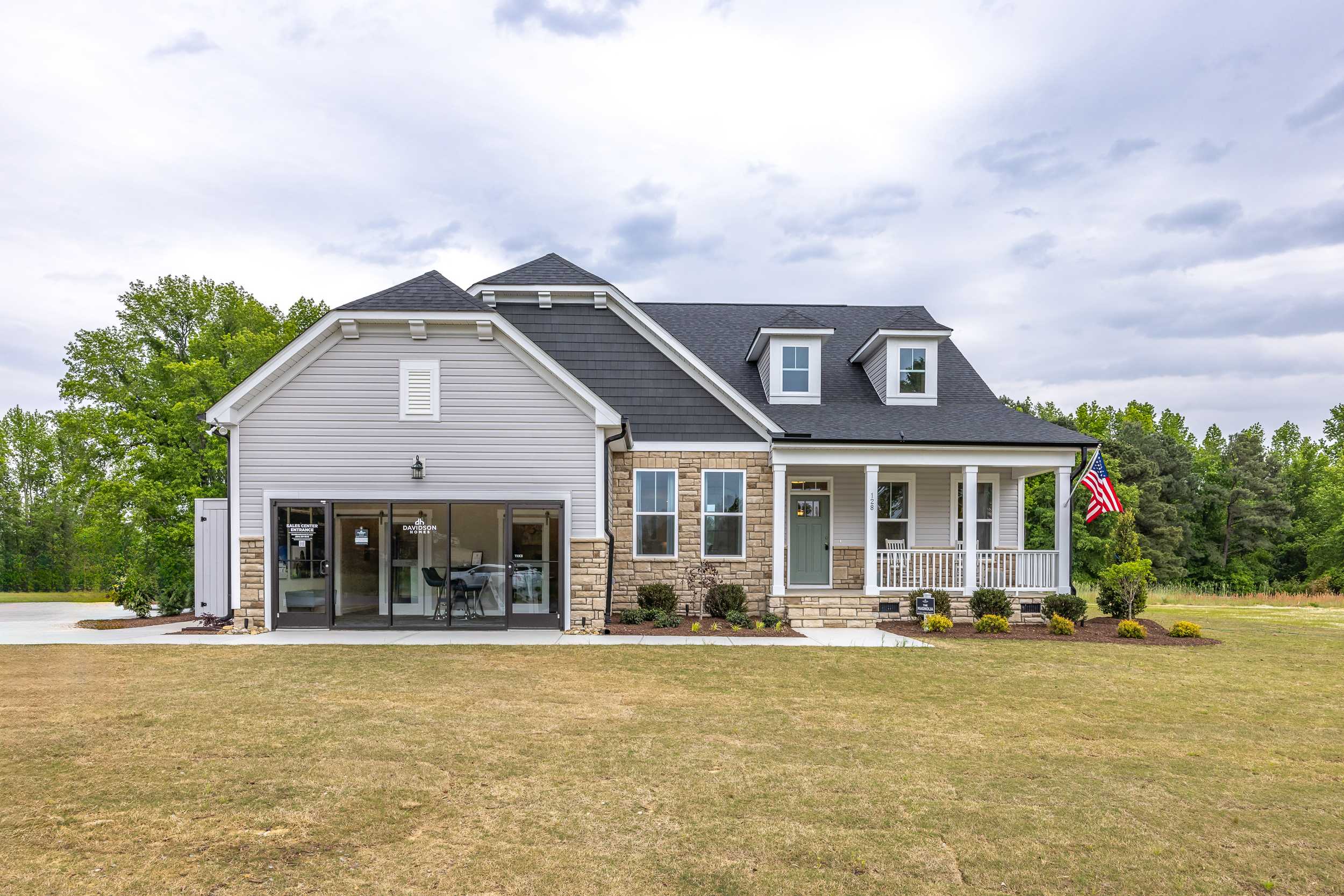 Charming two-story home exterior at Tobacco Road in Angier NC with white siding, black roof, covered porch, brick accents, and attached garage