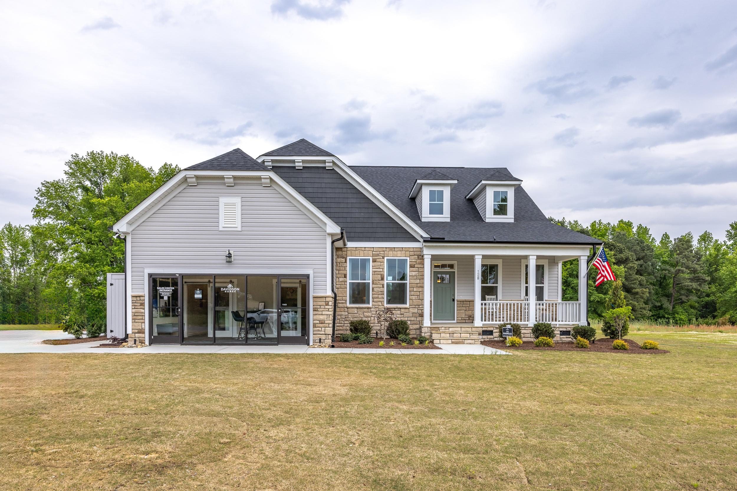 Charming two-story home exterior at Tobacco Road in Angier NC with white siding, black roof, covered porch, brick accents, and attached garage