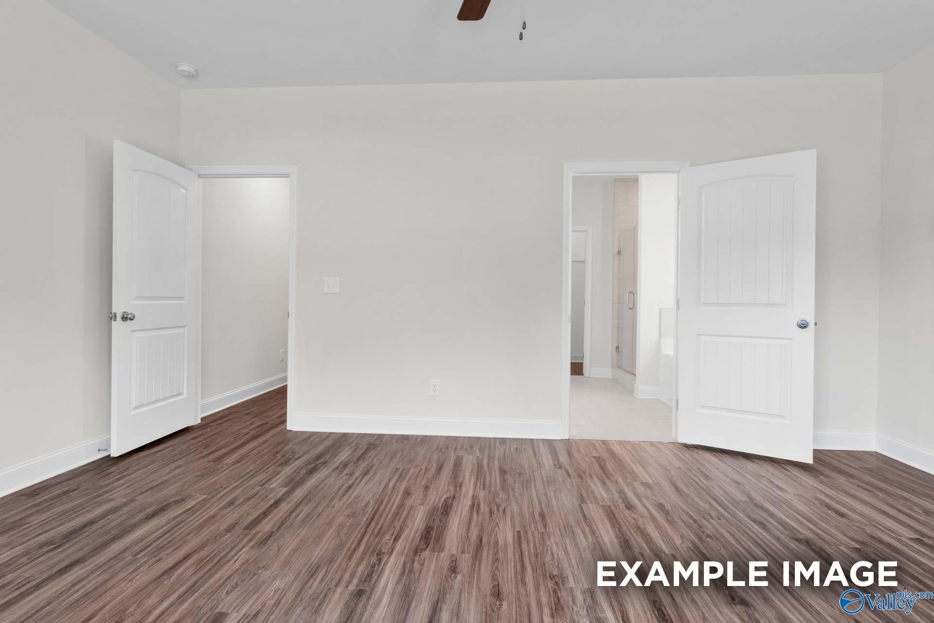 Spacious bedroom with hardwood floors, ceiling fan, and open doors to adjacent bath in Davidson Homes Montgomery C, Harvest, AL