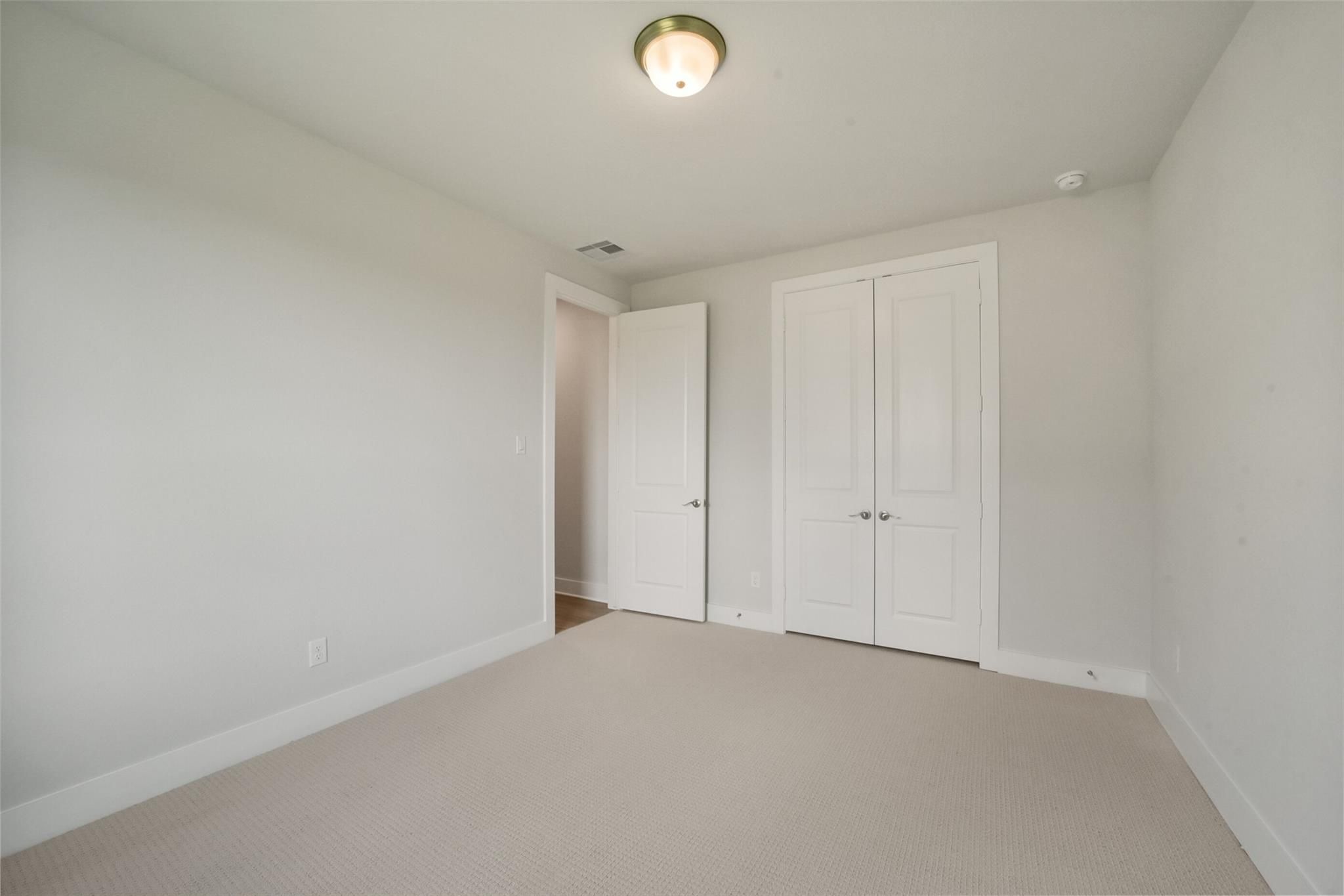 Spacious bedroom with white walls, beige carpet, double closet doors, and ceiling light in Davidson Homes The Zion A, Lago Mar, Texas City