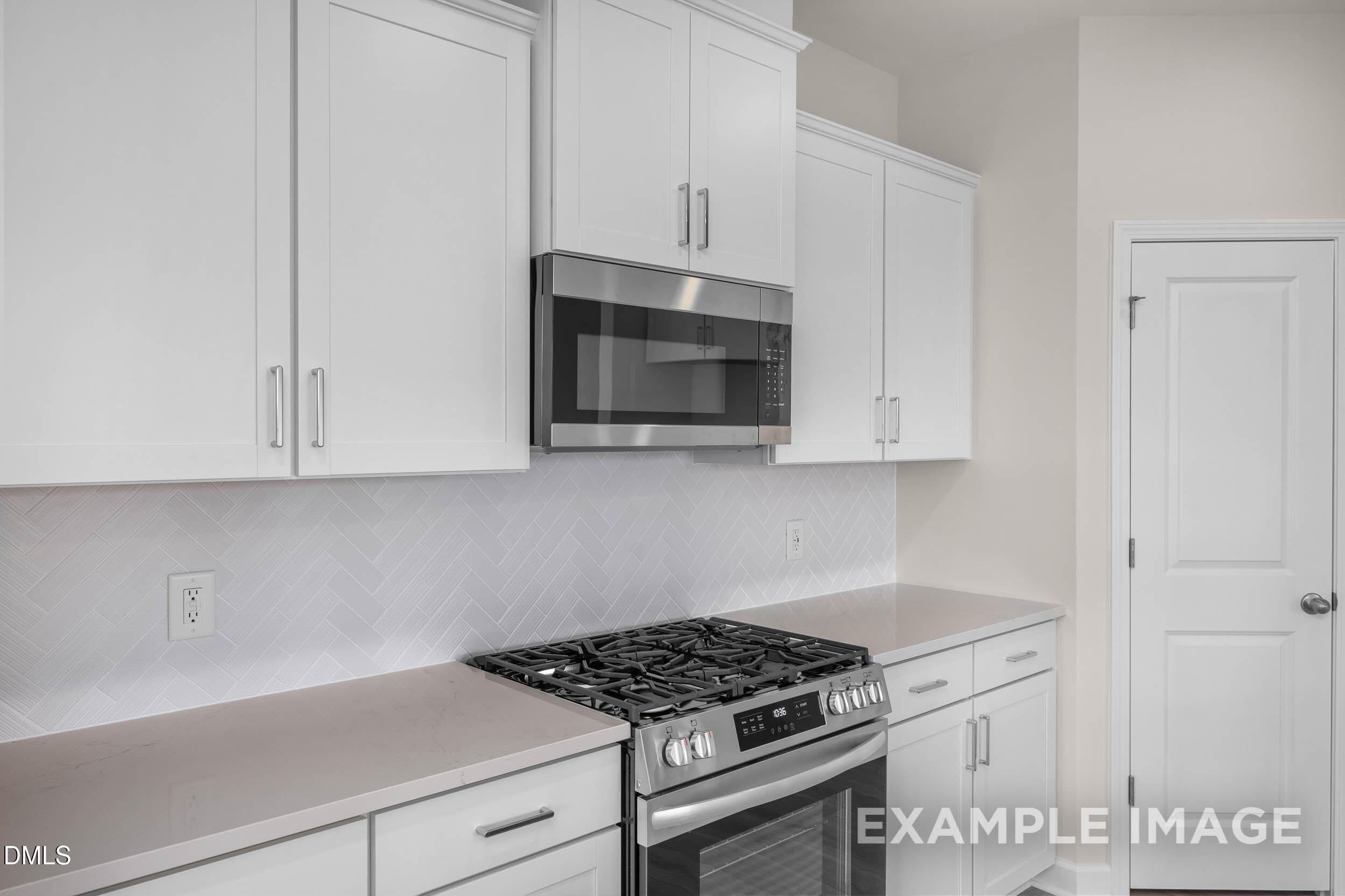 Modern kitchen with white cabinets, stainless steel appliances, and herringbone backsplash in The Franklin C floor plan.