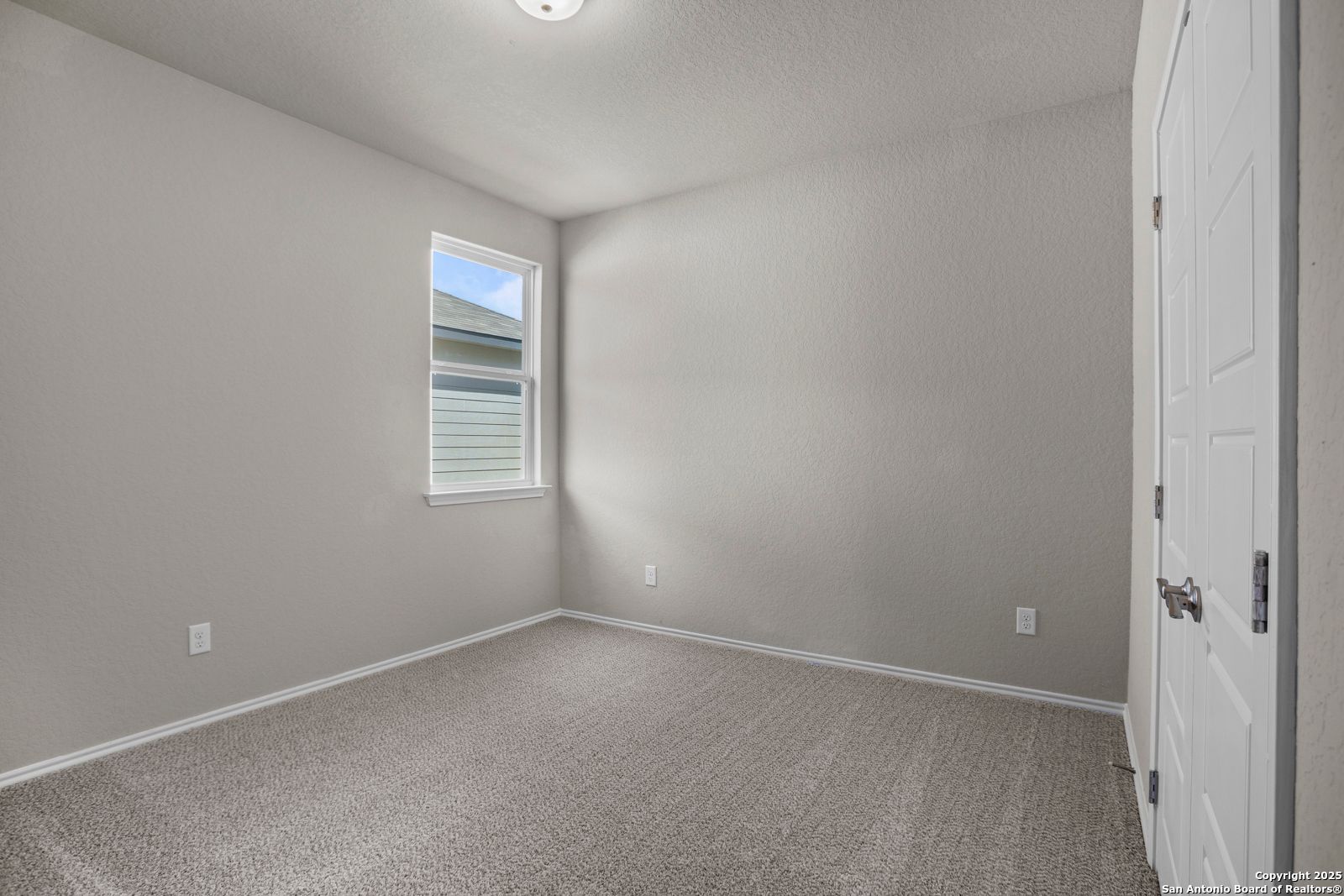Bright secondary bedroom with light gray walls, beige carpet, and window view in The Collin B home, Seguin, Texas