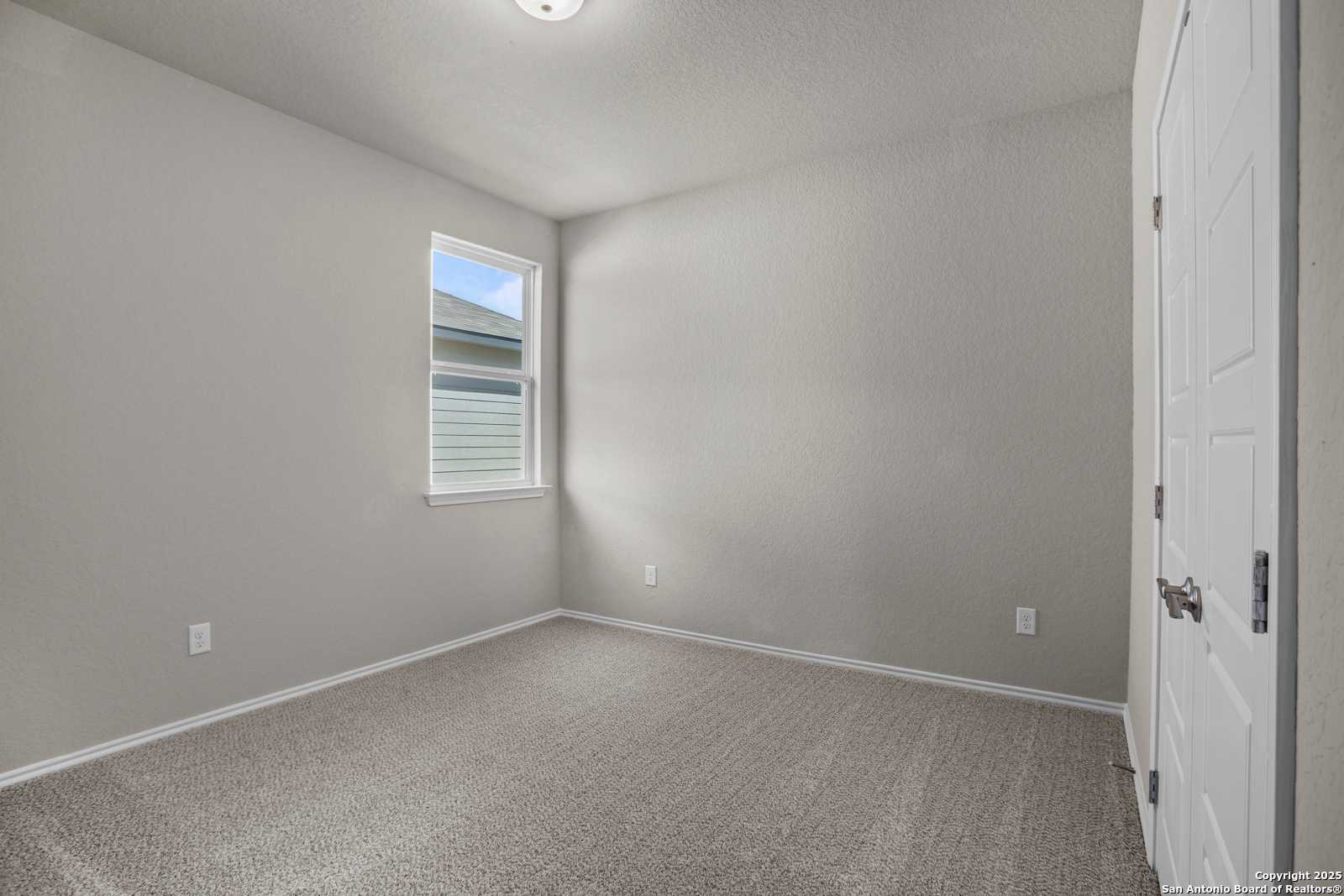 Bright secondary bedroom with light gray walls, beige carpet, and window view in The Collin B home, Seguin, Texas