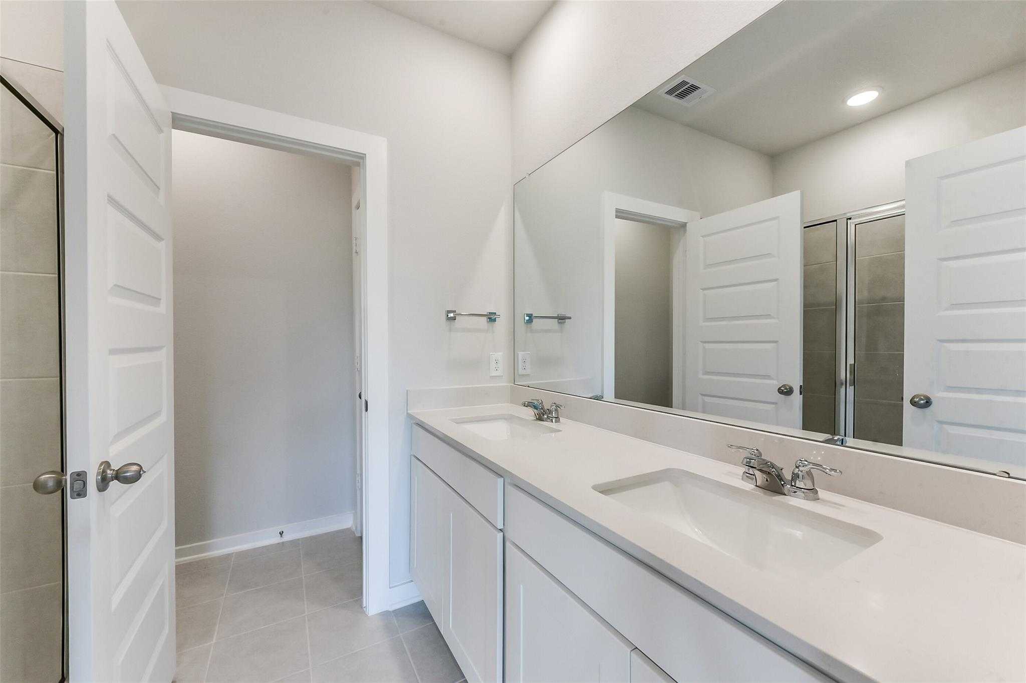 Modern master bathroom featuring double vanity sinks, large mirrors, and glass shower door in Davidson Homes The Frio F, Dayton, Texas