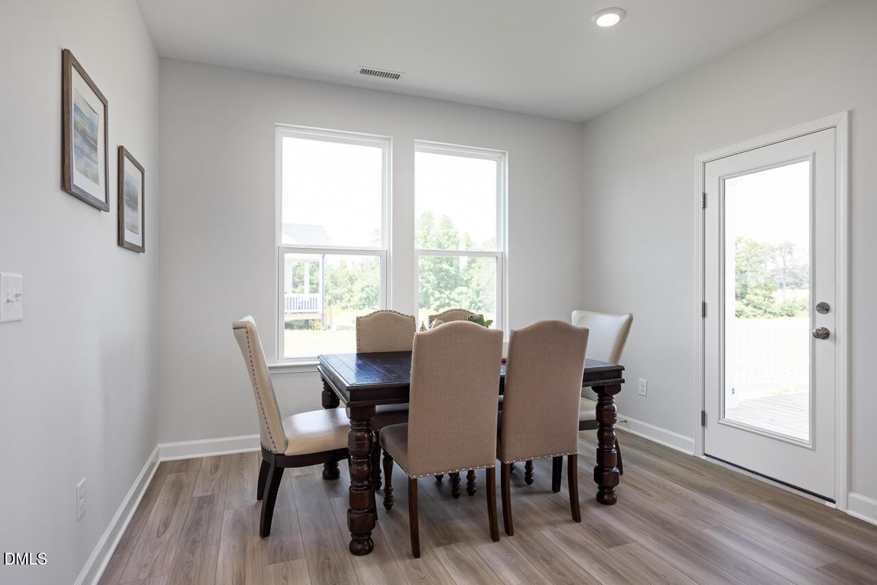 Sunlit dining room with wooden table, upholstered chairs, and large windows in The Daphne D by Davidson Homes, Lillington, NC