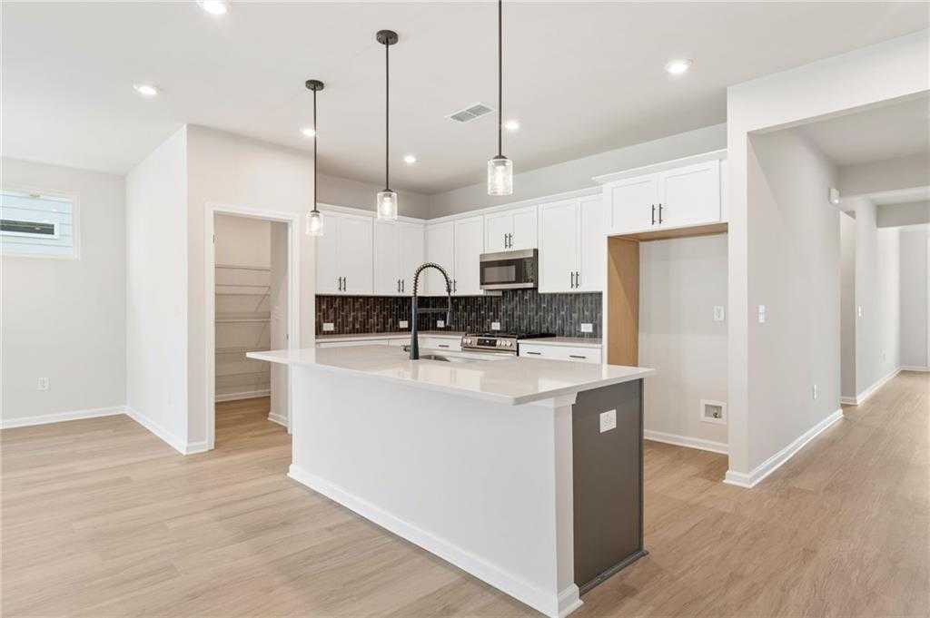 Modern white kitchen with shaker cabinets, quartz island, black faucet, stainless microwave, and hardwood floors in Davidson Homes The Daphne C, Loganville