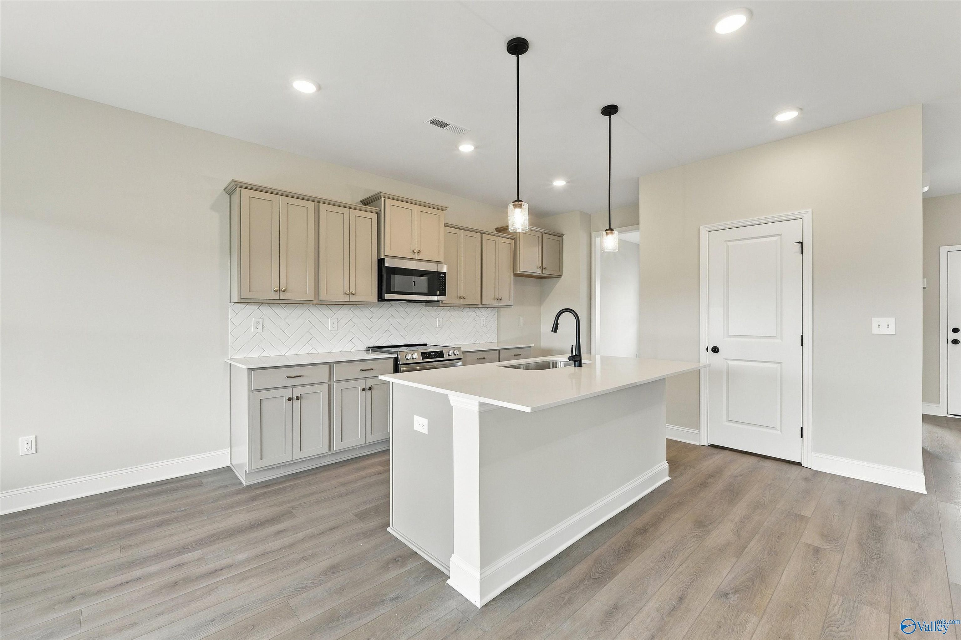 Modern kitchen with large island, pendant lights, and herringbone backsplash in Davidson Homes The Shelby A, Athens, Alabama