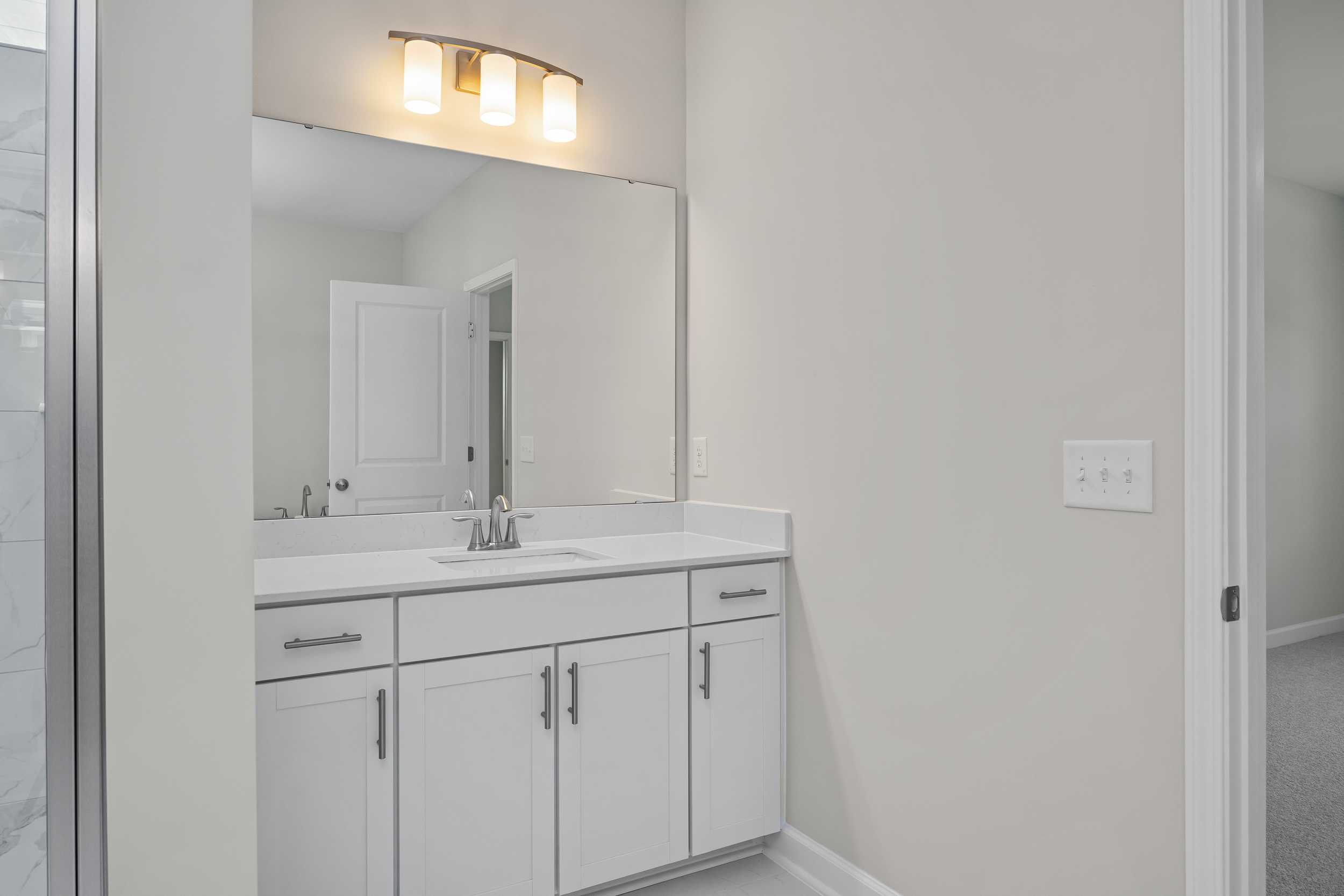 Spacious master bathroom in The Aspen C featuring white shaker vanity, single sink, large mirror, and glass shower enclosure