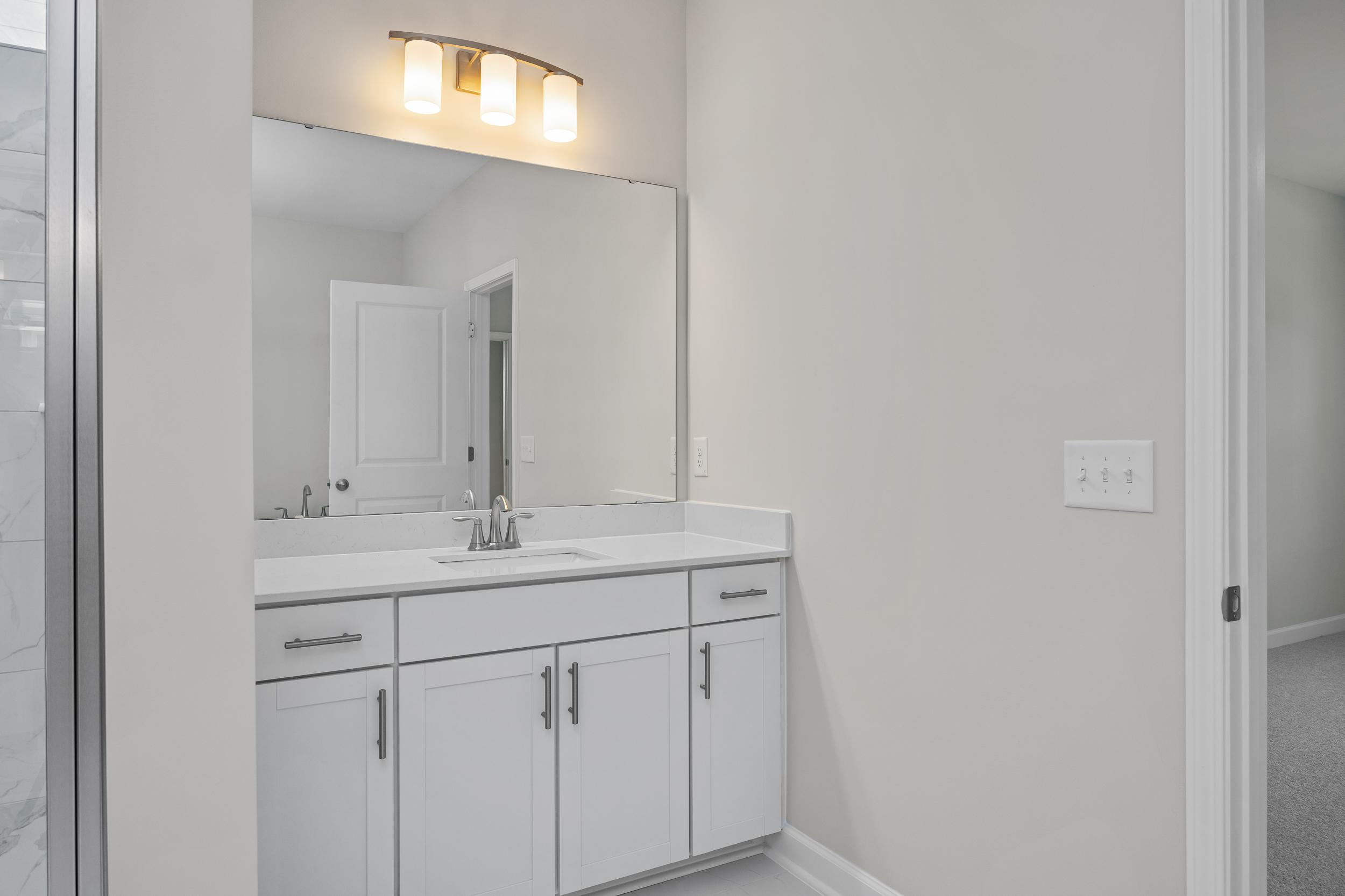Spacious master bathroom in The Aspen C featuring white shaker vanity, single sink, large mirror, and glass shower enclosure