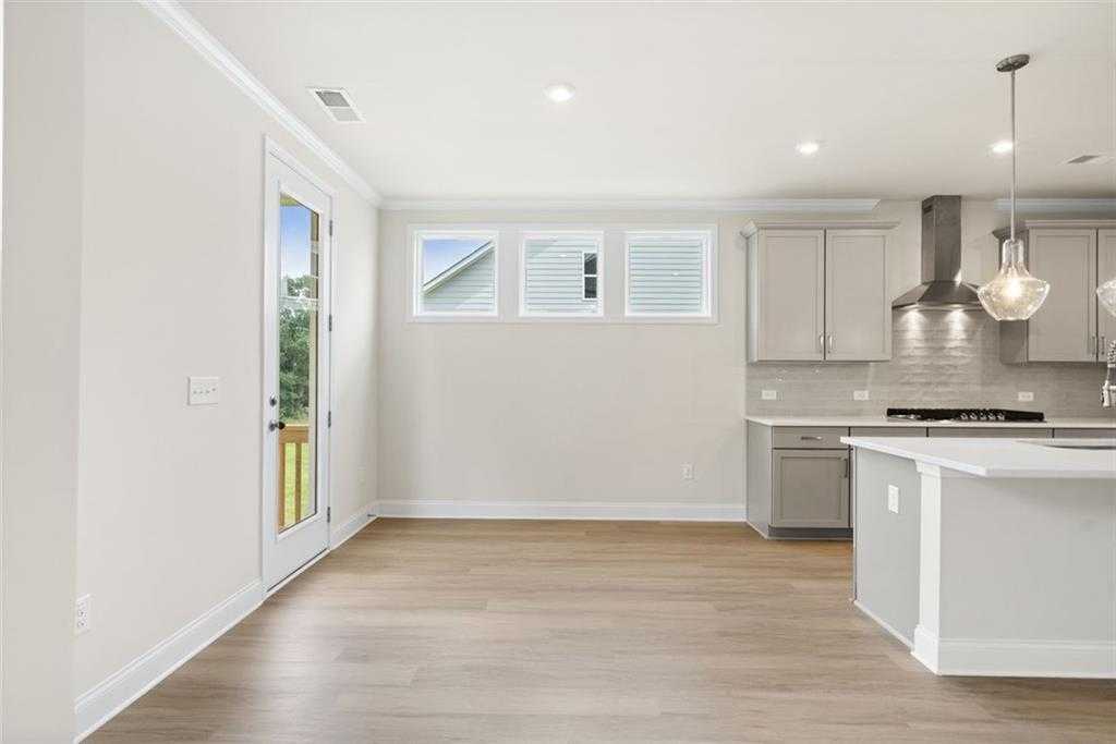 Bright open-concept kitchen with white cabinets, stainless appliances, island, and sliding doors to deck in The Willow D home, Wehunt Meadows, Hoschton