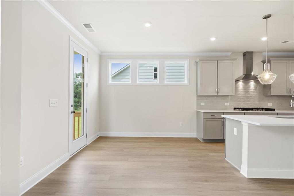 Bright open-concept kitchen with white cabinets, stainless appliances, island, and sliding doors to deck in The Willow D home, Wehunt Meadows, Hoschton