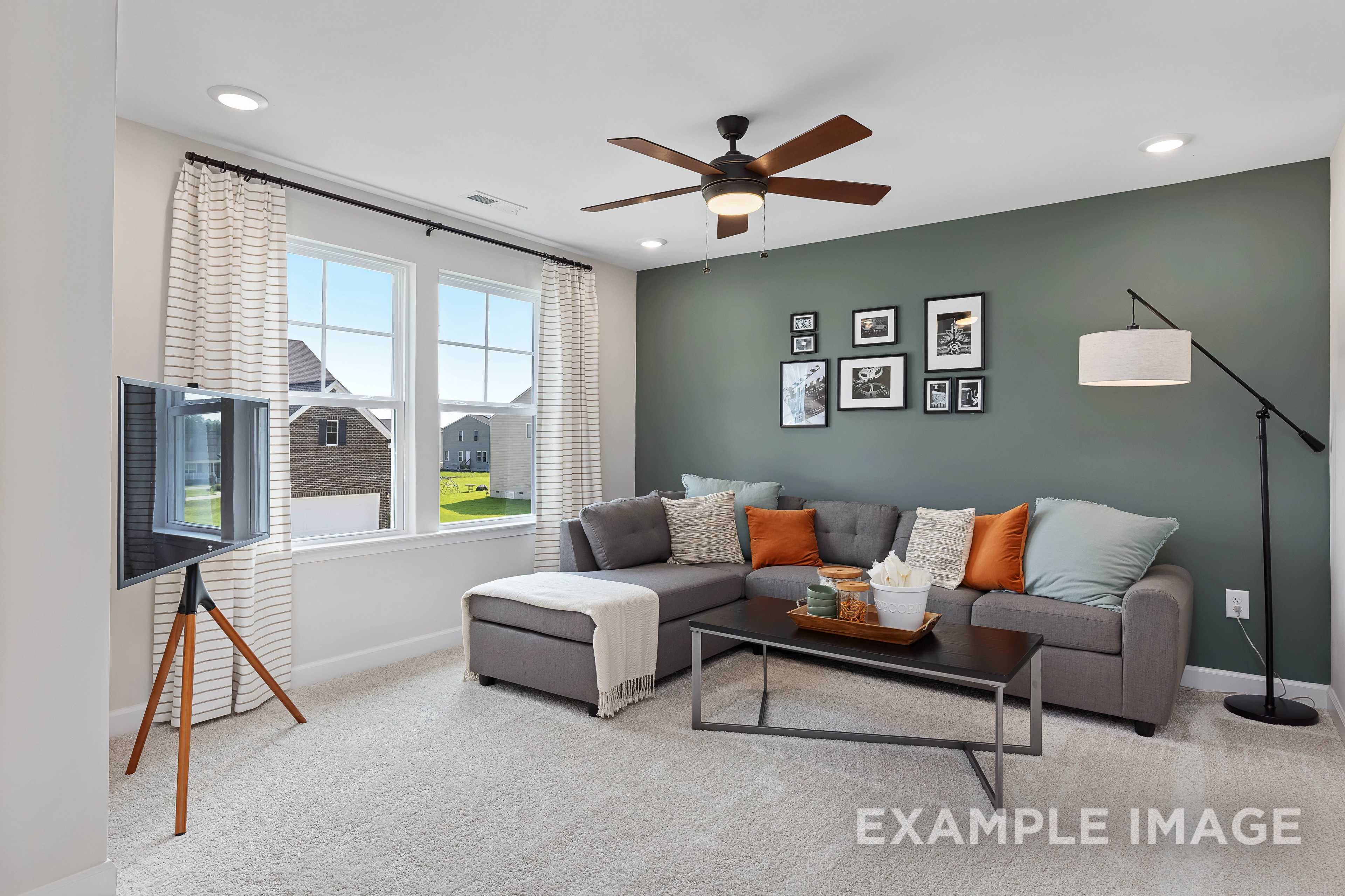 Cozy upstairs family room in The Willow B by Davidson Homes featuring gray L-shaped sofa, orange accents, ceiling fan, and large windows with green views