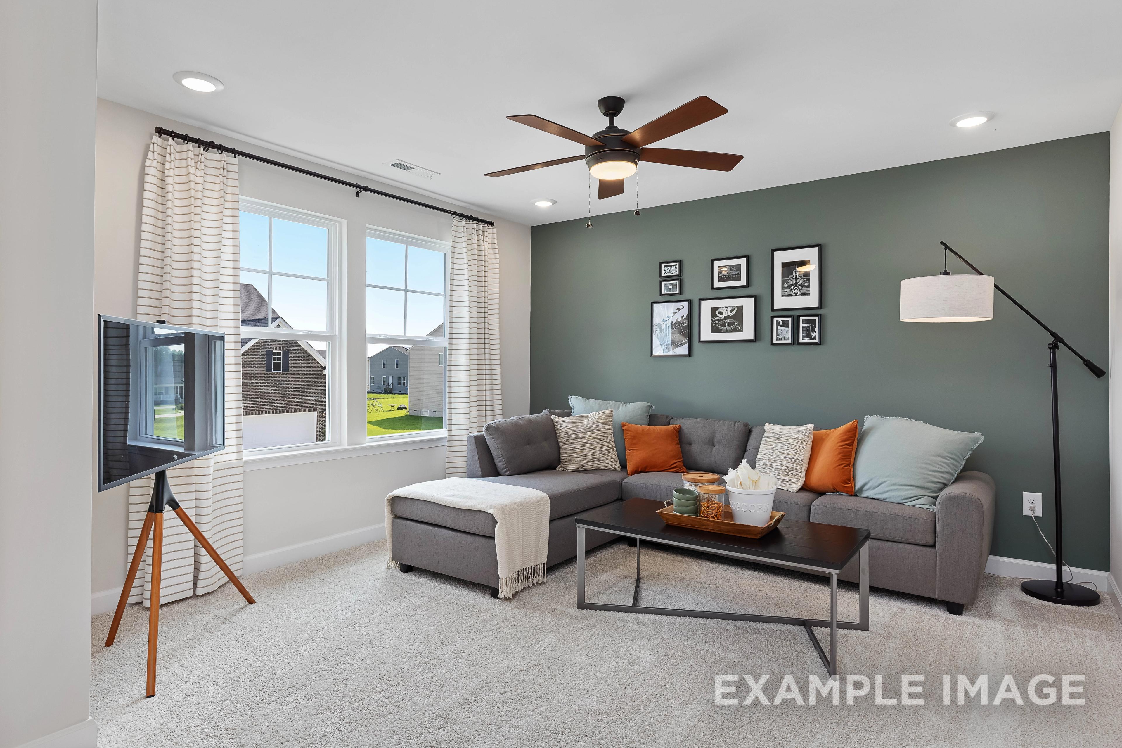 Cozy upstairs family room in The Willow B by Davidson Homes featuring gray L-shaped sofa, orange accents, ceiling fan, and large windows with green views