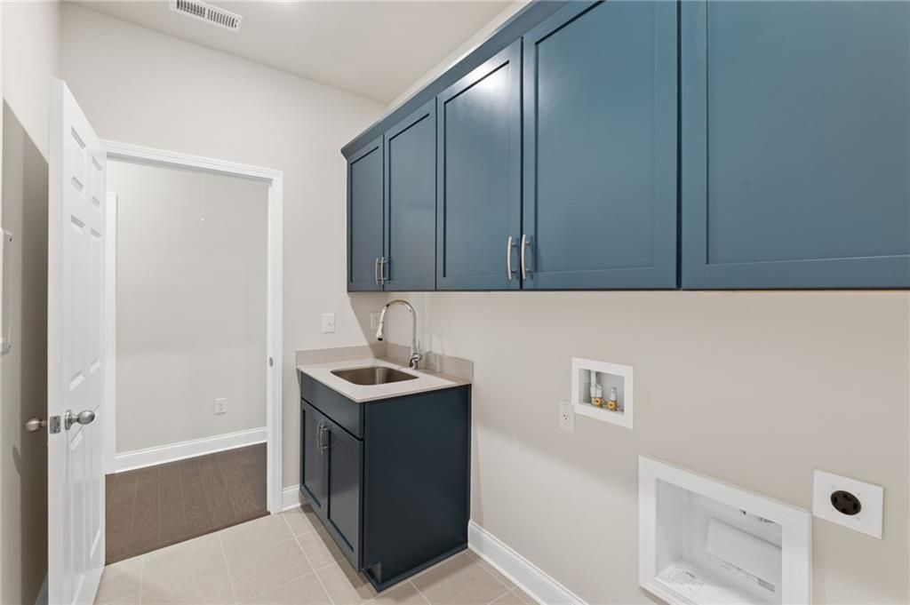 Modern laundry room with navy blue cabinets, utility sink, and washer-dryer hookups in Davidson Homes The Harrison G, Hoschton, Georgia