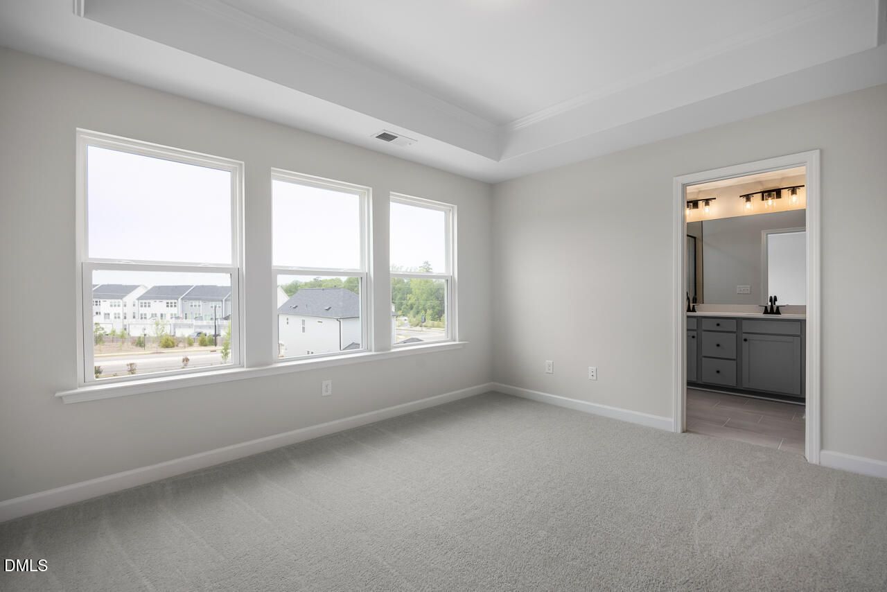Bright primary bedroom with tray ceiling and en suite bathroom in The Mitchell floor plan at Forestville Yard, Knightdale.