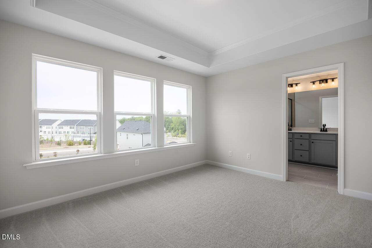 Bright primary bedroom with tray ceiling and en suite bathroom in The Mitchell floor plan at Forestville Yard, Knightdale.